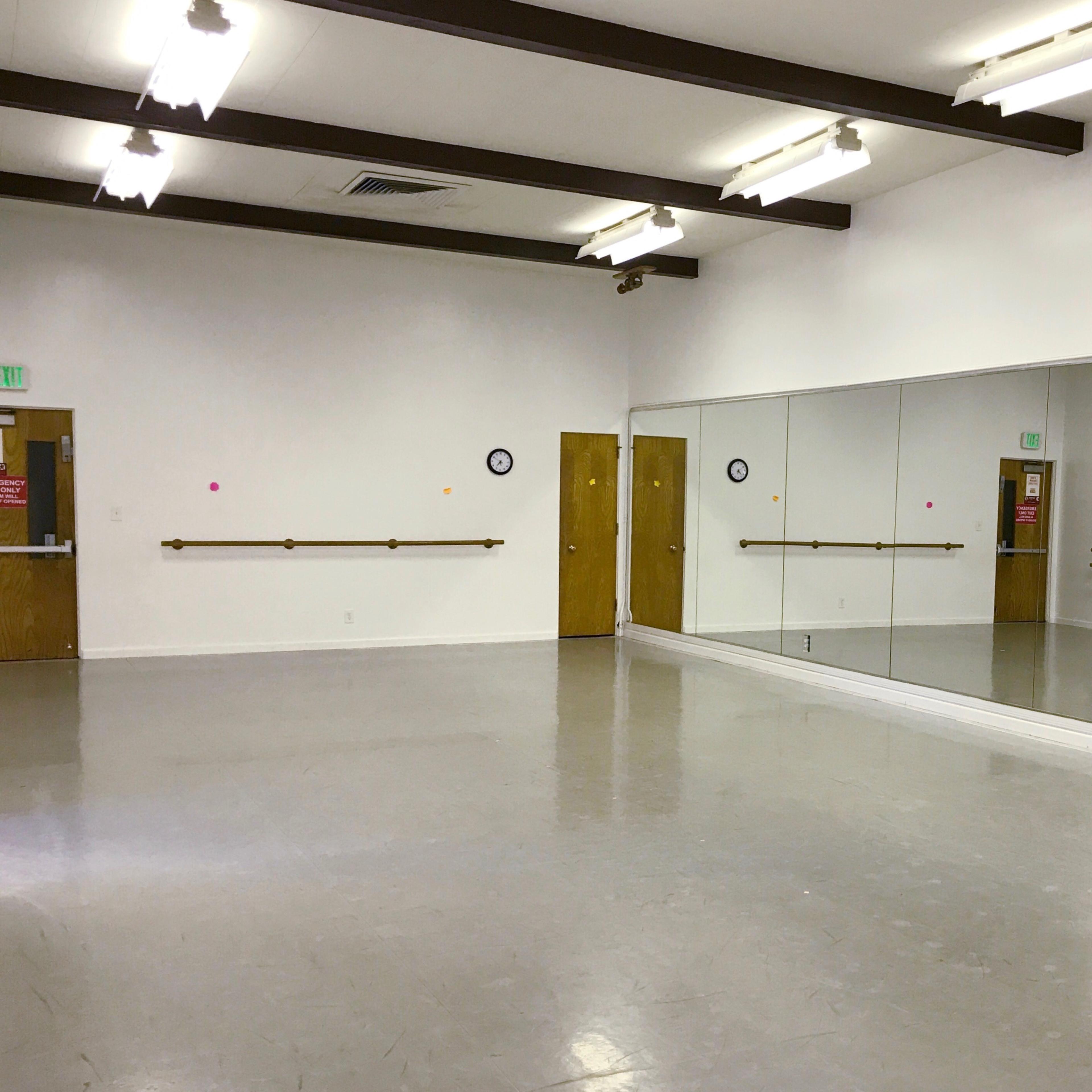 A spacious dance studio with mirrored walls, wooden barre, and two doors.