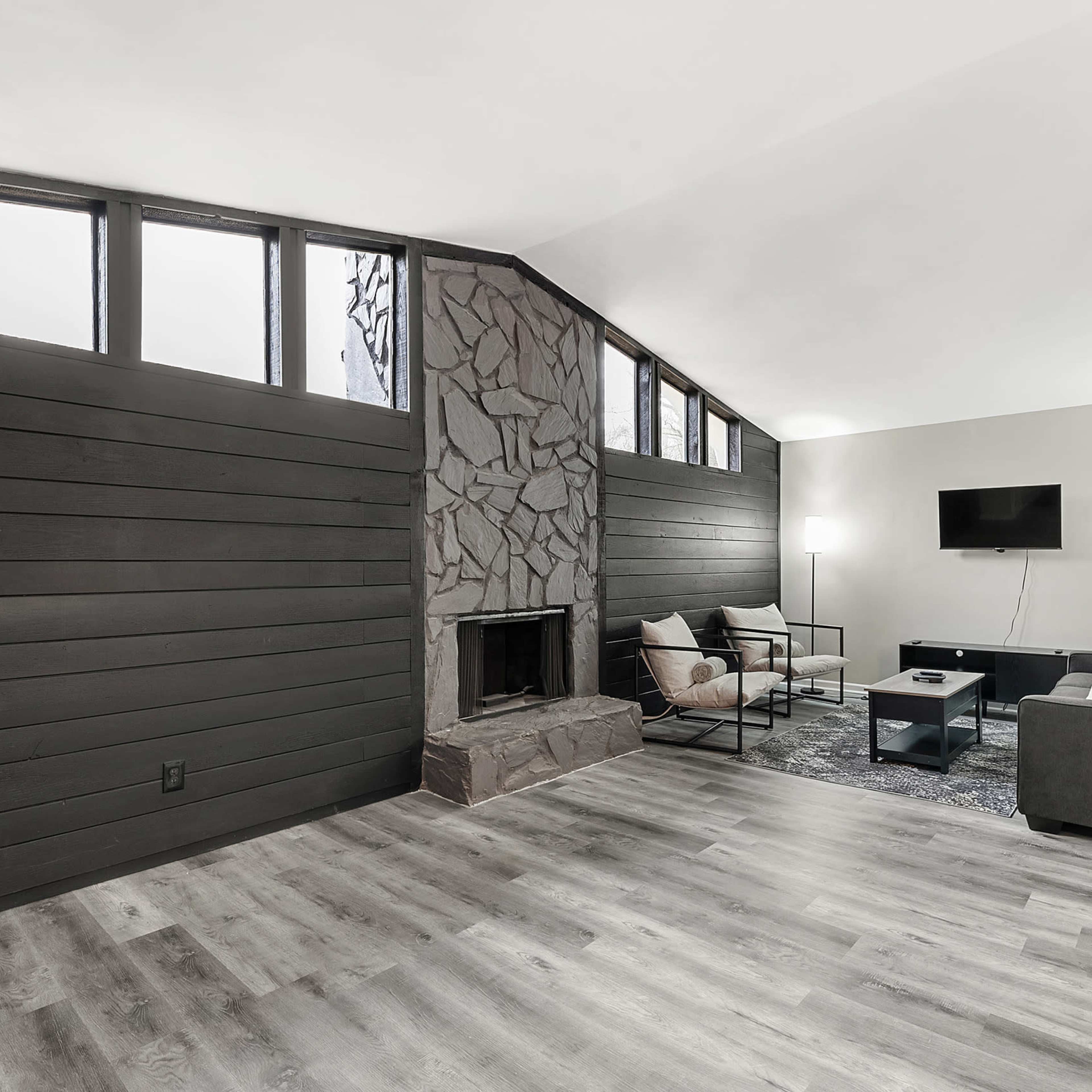 A modern living room featuring a stone fireplace, large windows, and minimalist furniture.