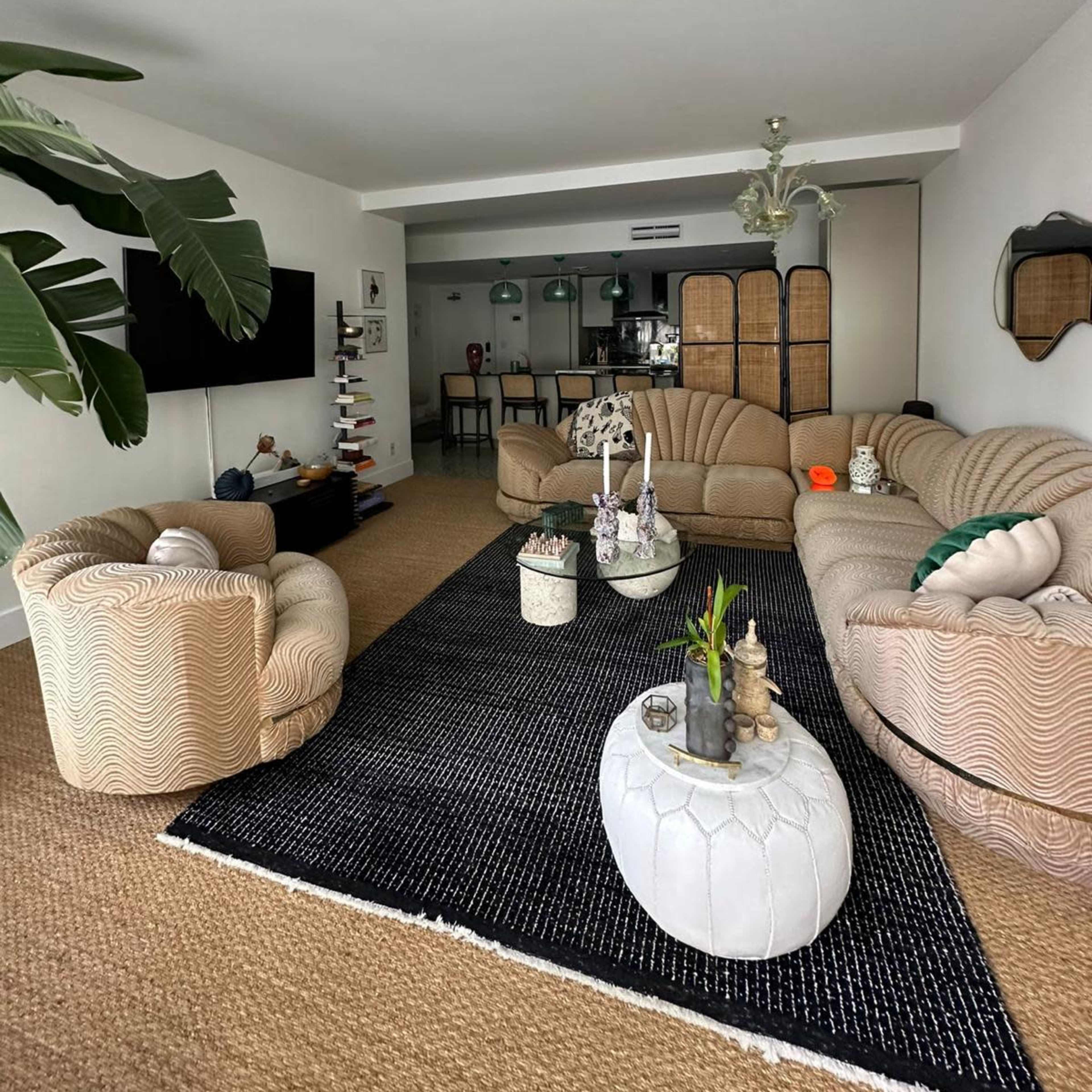 A modern living room featuring two curved sofas, a black area rug, a coffee table, and a dining area in the background.
