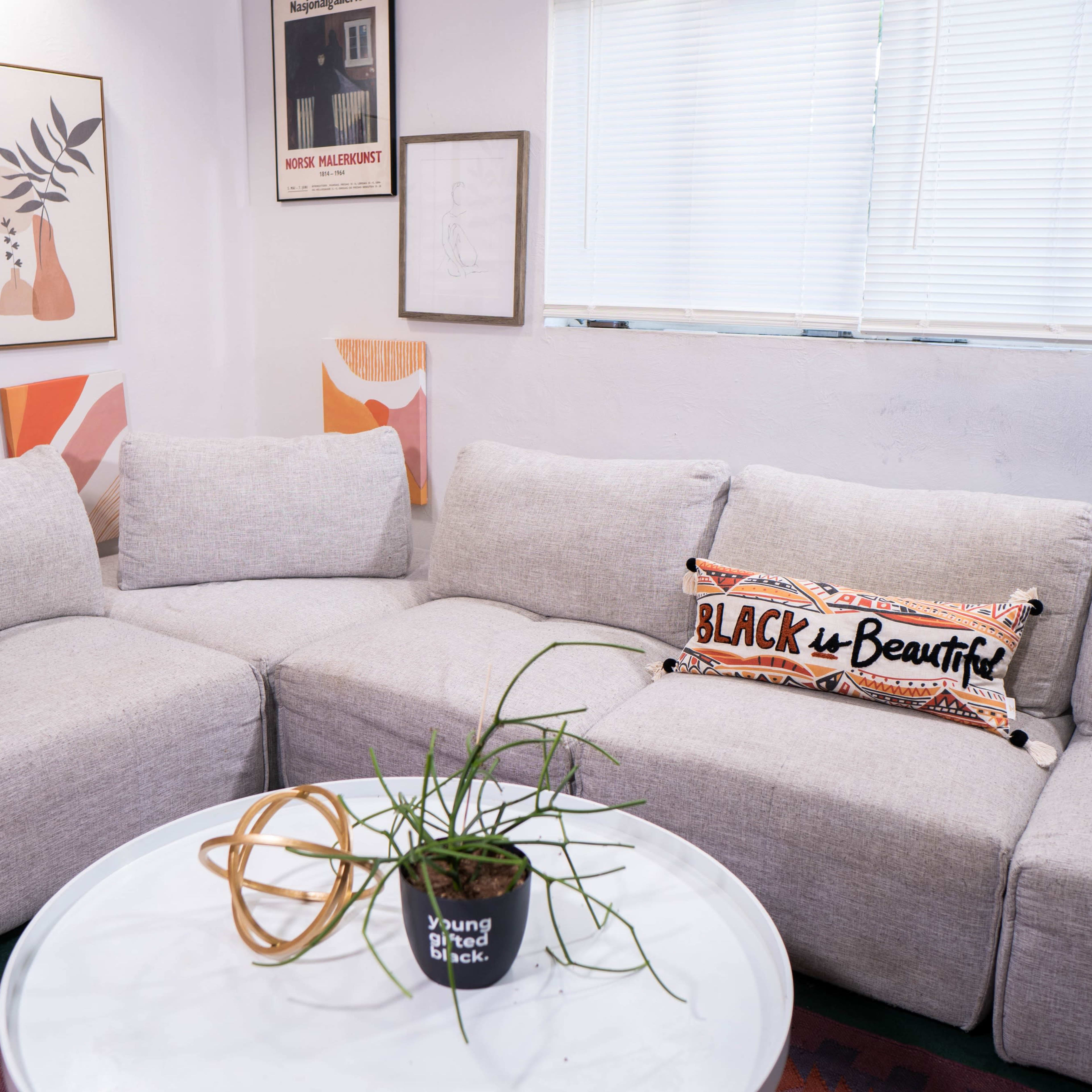 A light-colored sectional couch is arranged around a circular coffee table in a room decorated with framed wall art and a plant.