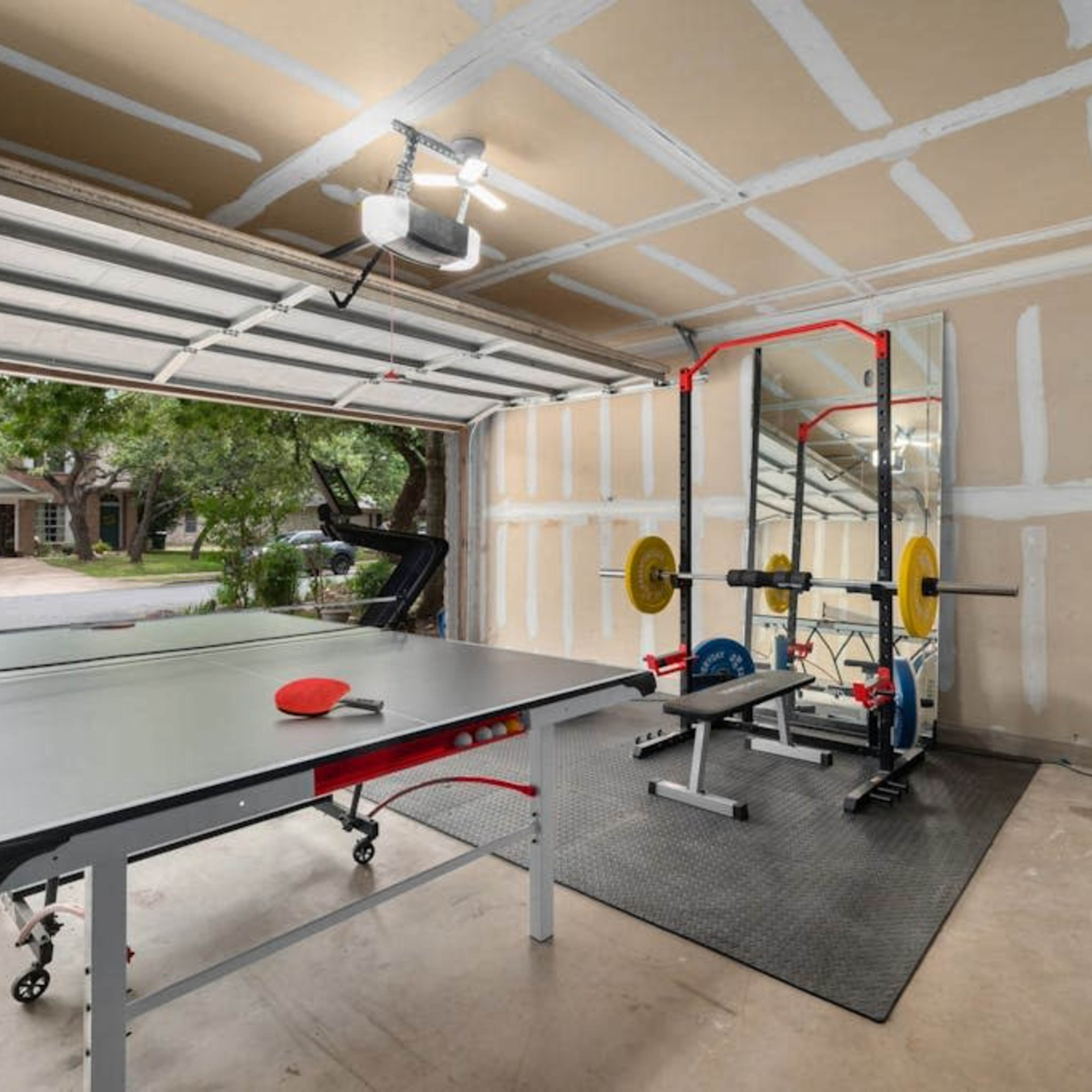A garage with a ping pong table, a weightlifting set, a mirror, and exercise equipment.