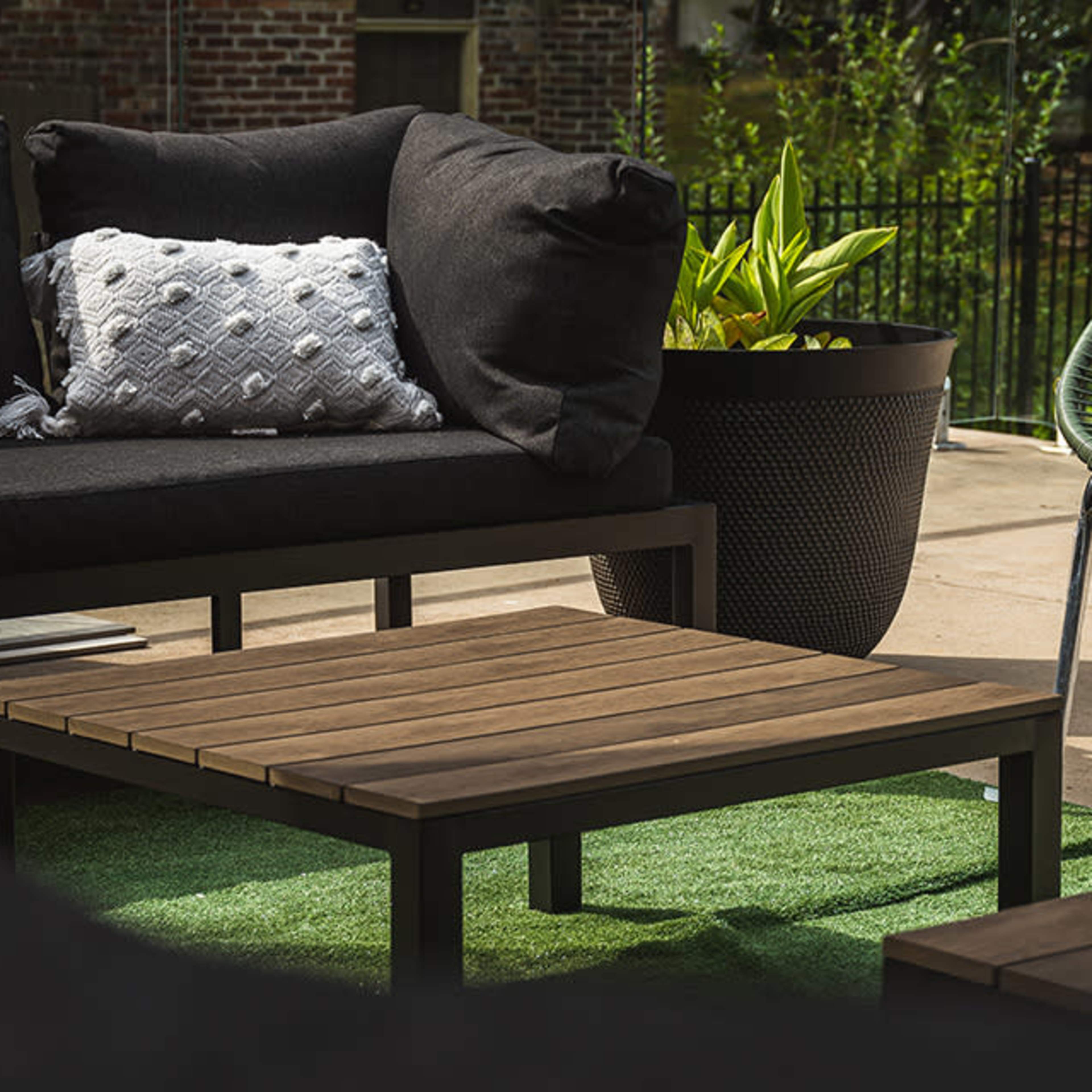 An outdoor seating area featuring a black sofa with a decorative pillow, a wooden coffee table, and a green chair next to a potted plant.