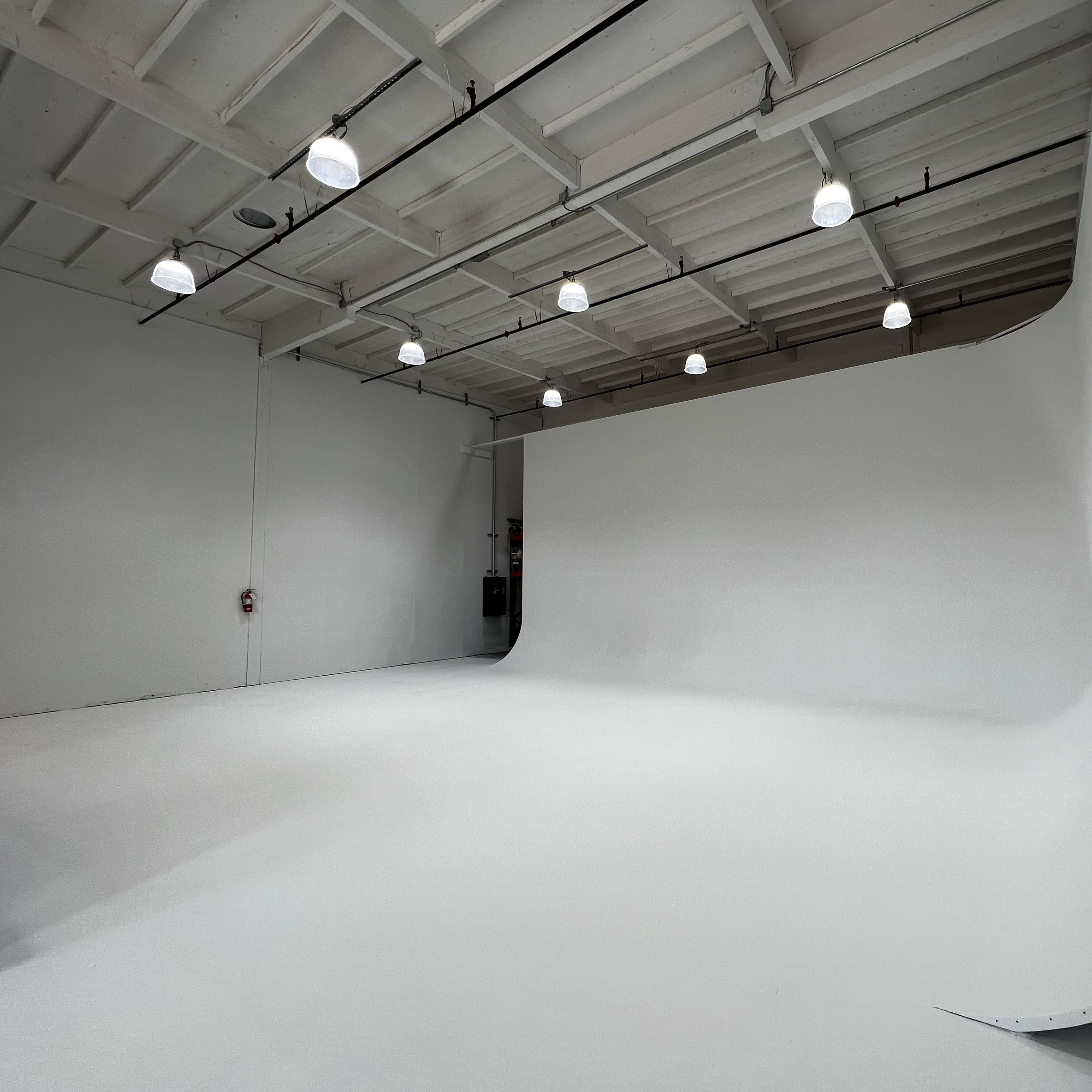 A spacious, empty photography studio with a white backdrop and overhead lights.