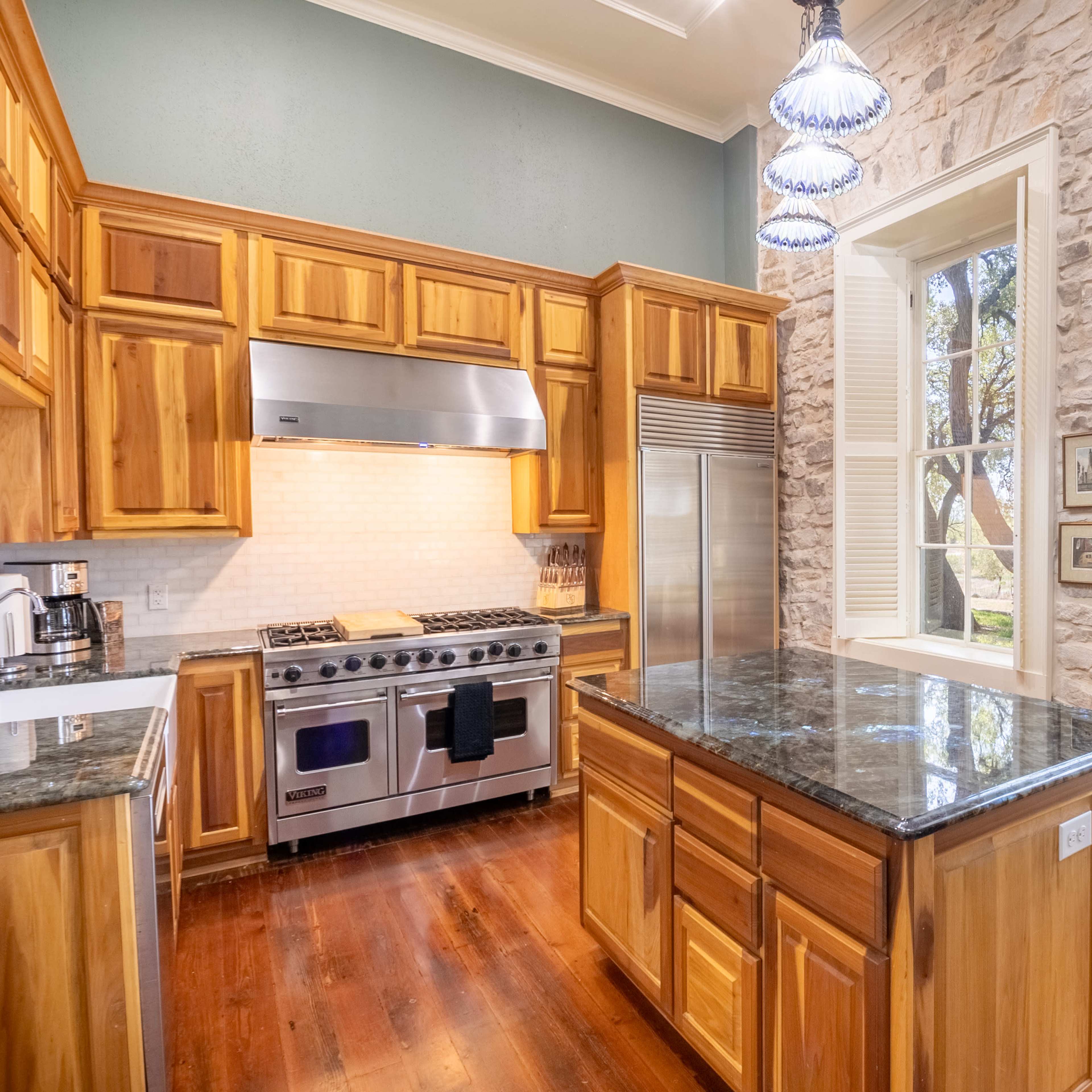 The kitchen features wooden cabinetry, a large island with a dark countertop, and a stainless steel stove beneath a hood, illuminated by pendant lights.