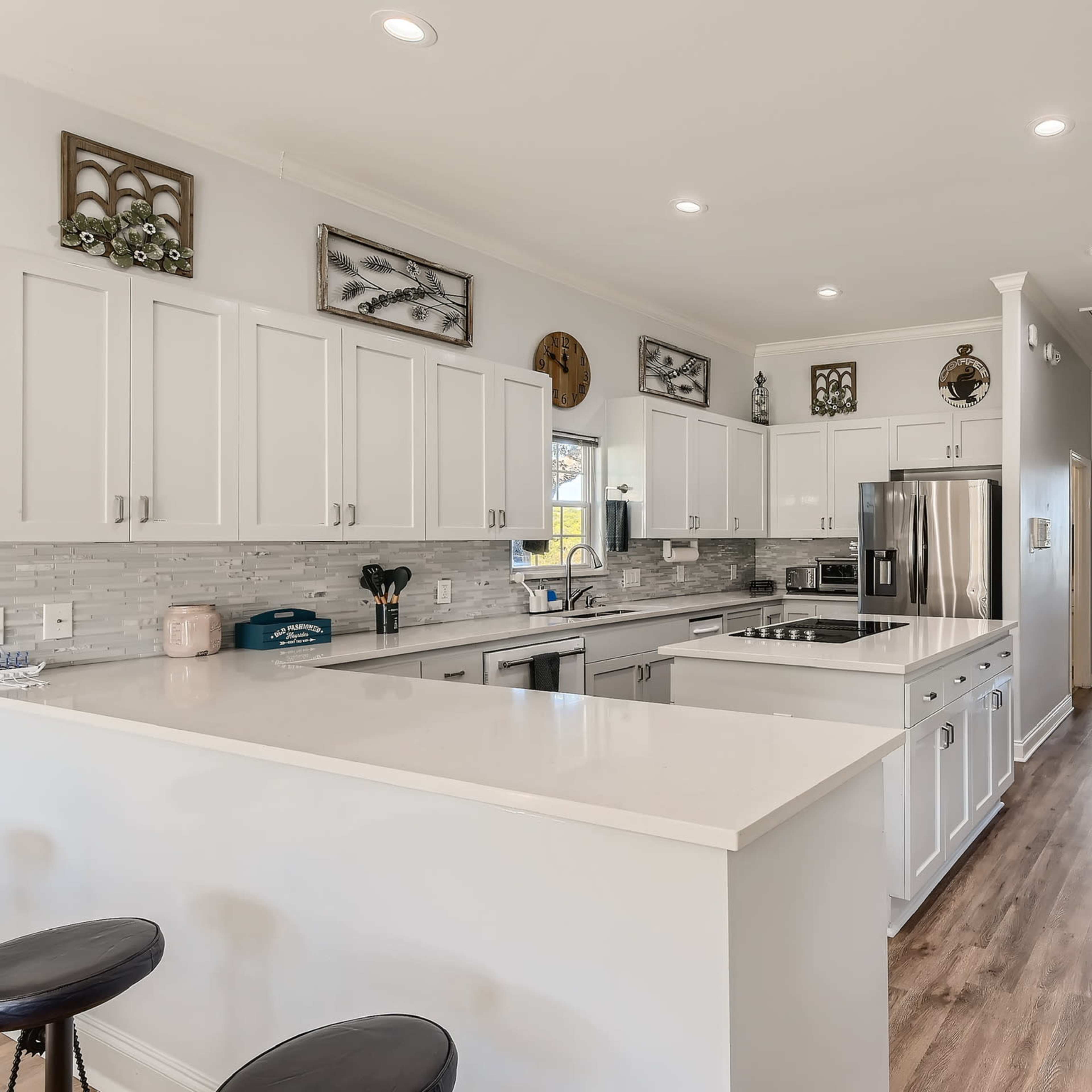 A spacious modern kitchen with white cabinetry, a central island, and stainless steel appliances, leading to a well-lit hallway.