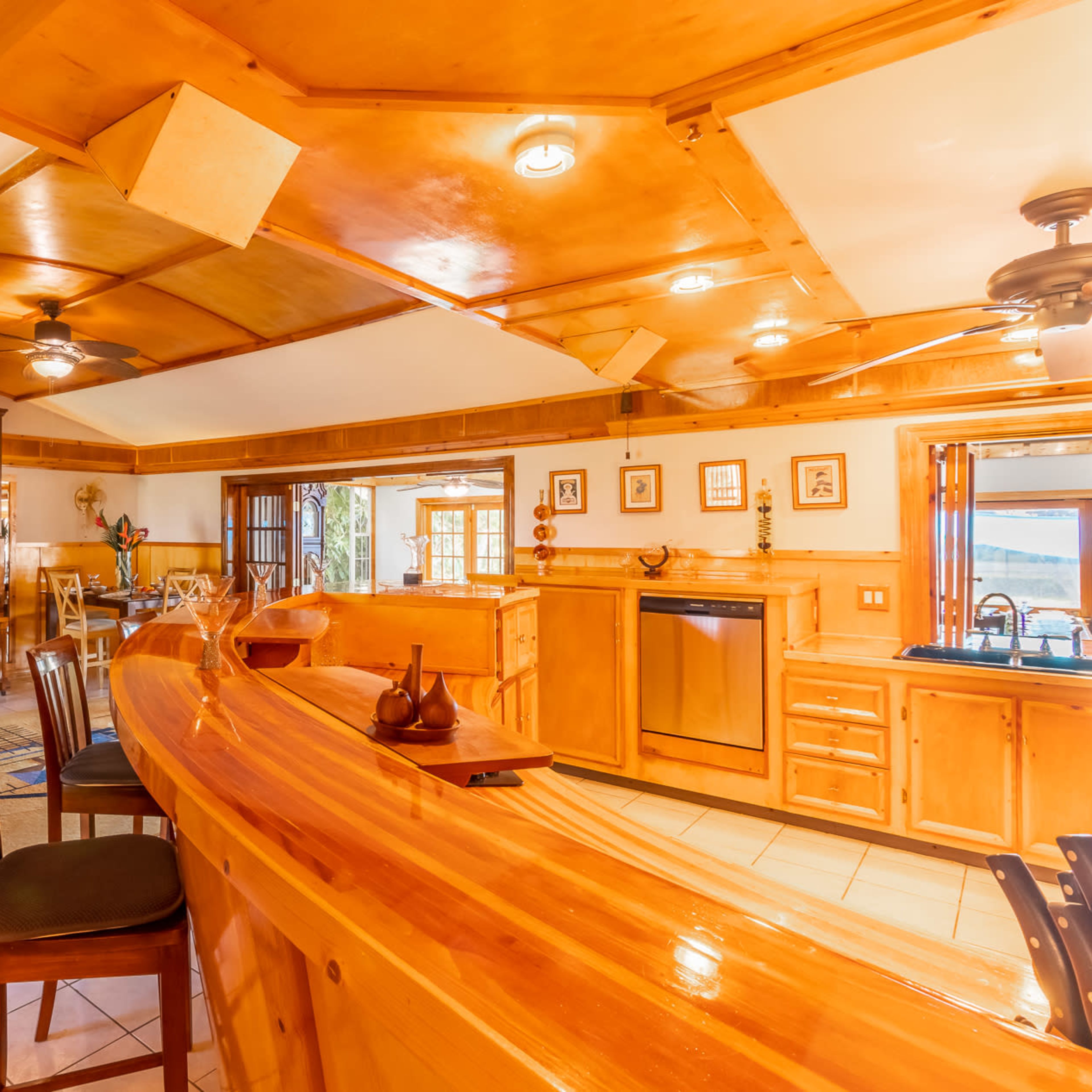 A wooden bar area with high stools, a piano in the corner, and a spacious kitchen featuring cabinets and a window overlooking a scenic view.