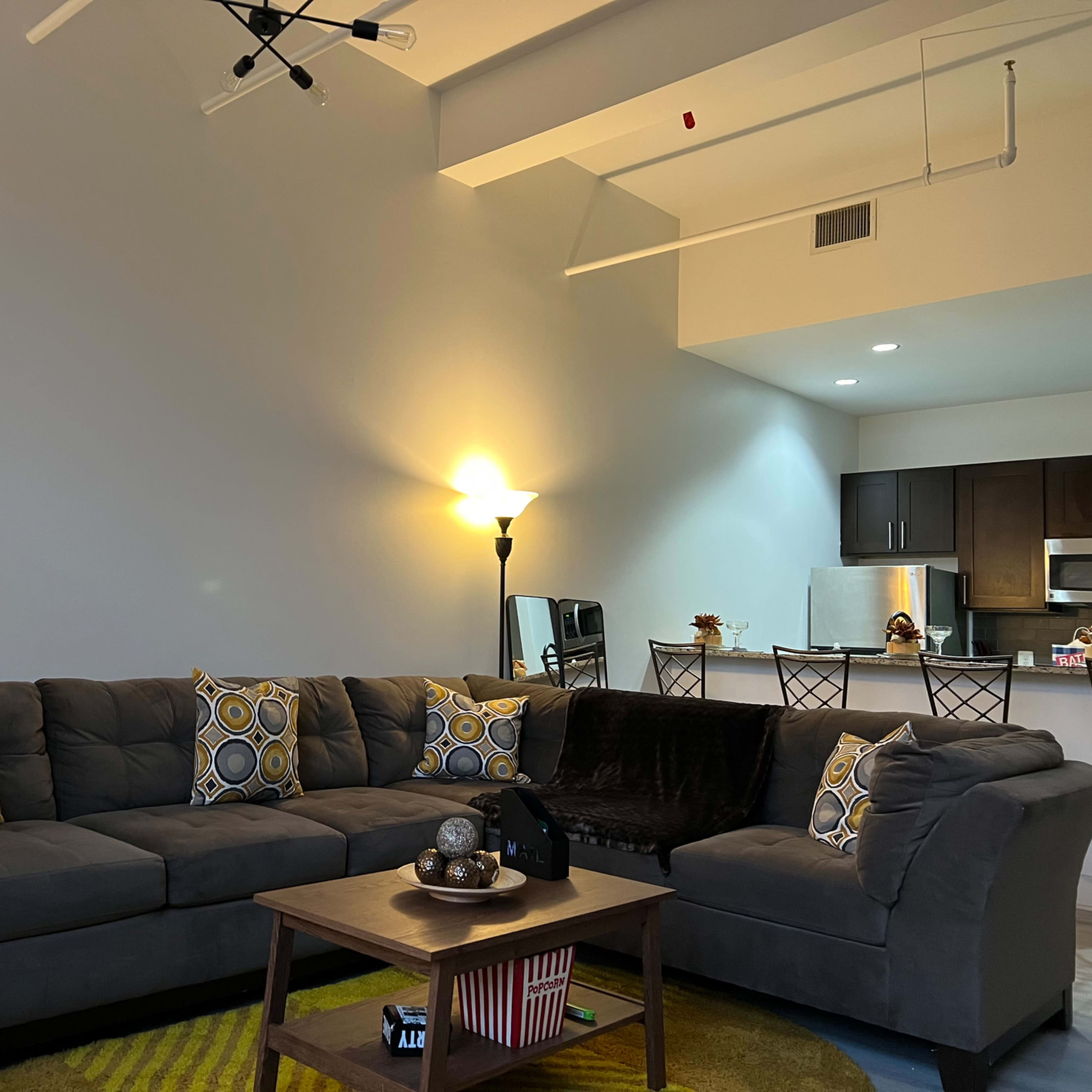 A modern living room with a sectional gray sofa, a coffee table, and a kitchen area in the background.