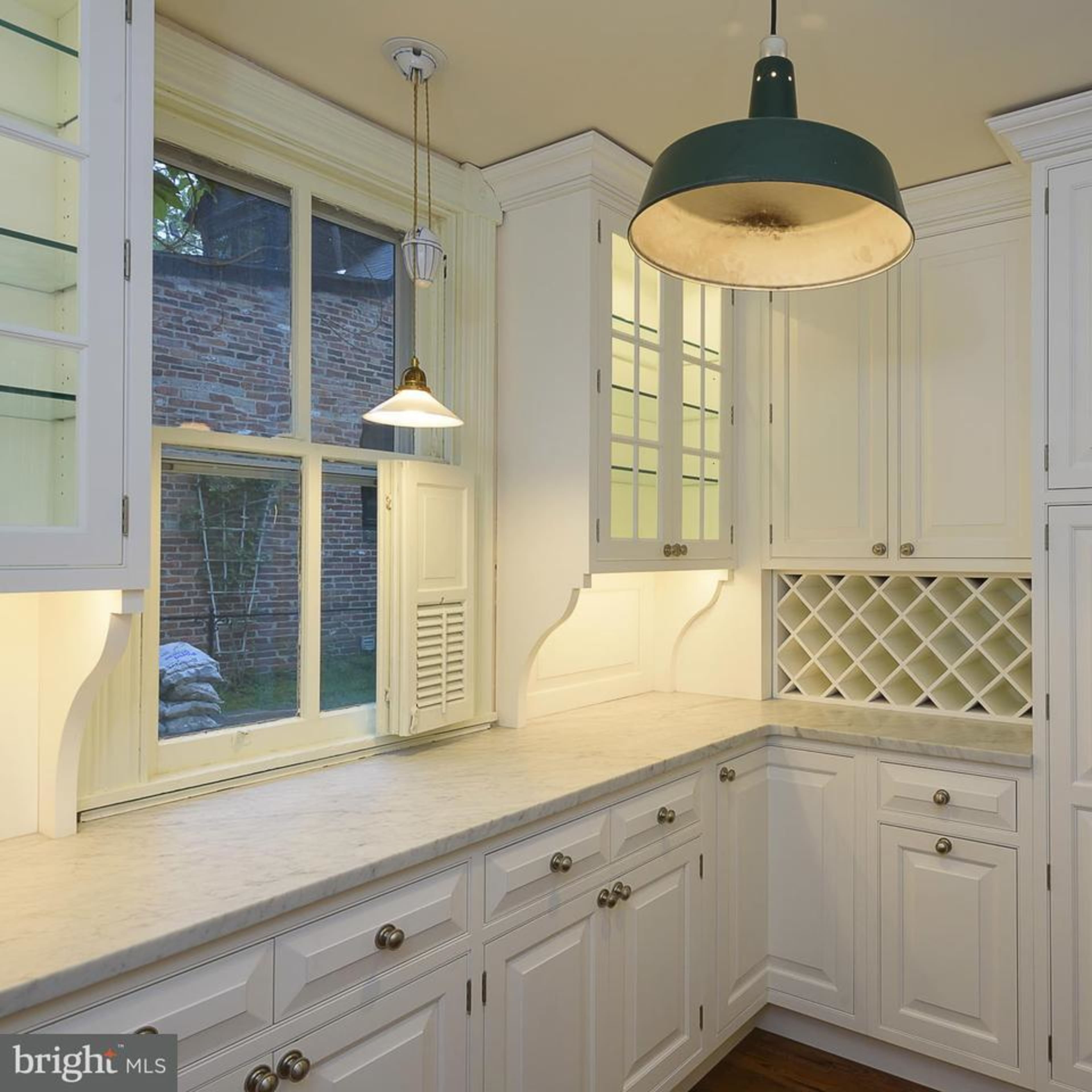 A kitchen with white cabinetry, a marble countertop, and large windows allowing natural light.