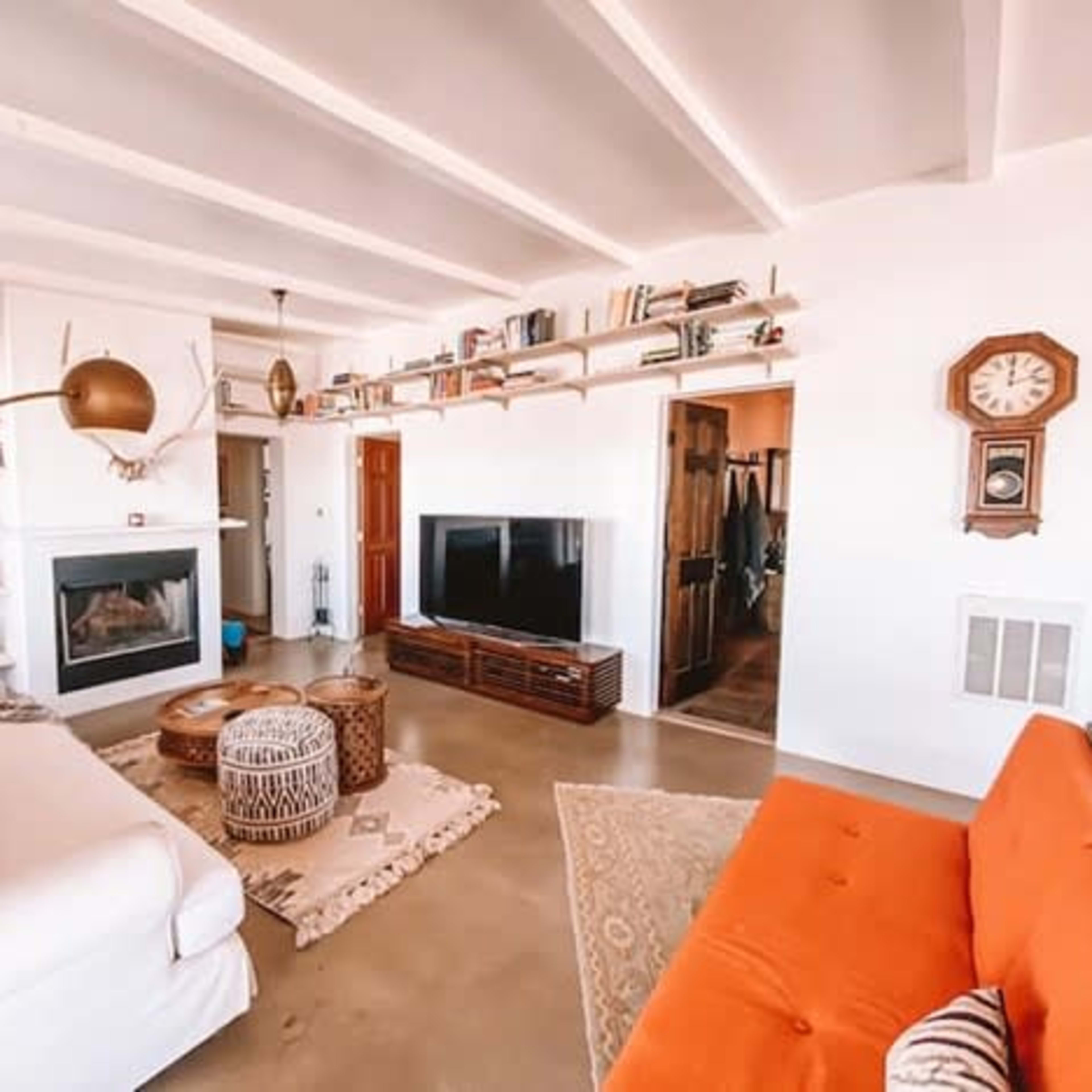 The living room features a white sectional sofa, an orange couch, a large television, a fireplace, and bookshelves filled with books.