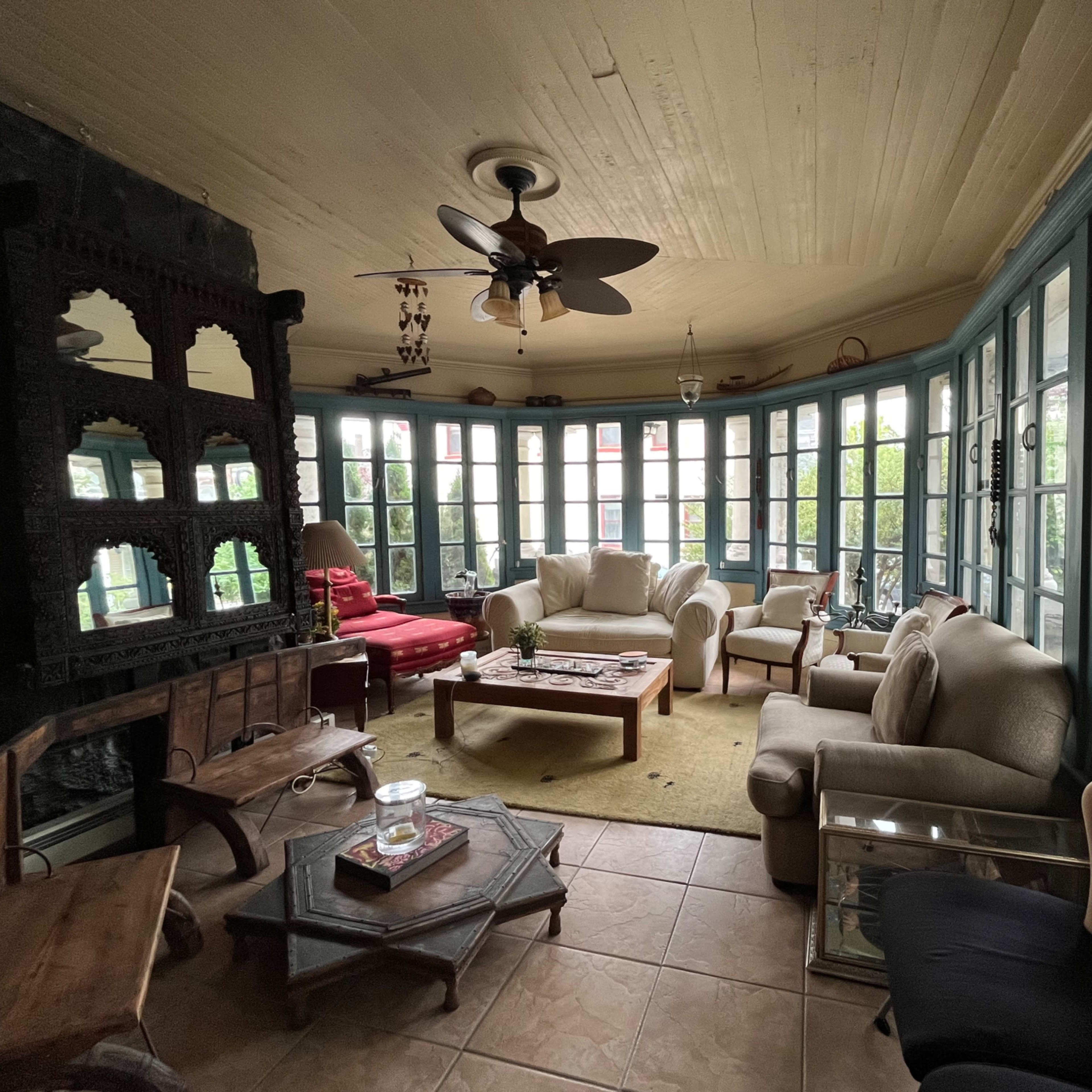 A sunroom filled with various seating arrangements, large windows, and a stone fireplace.