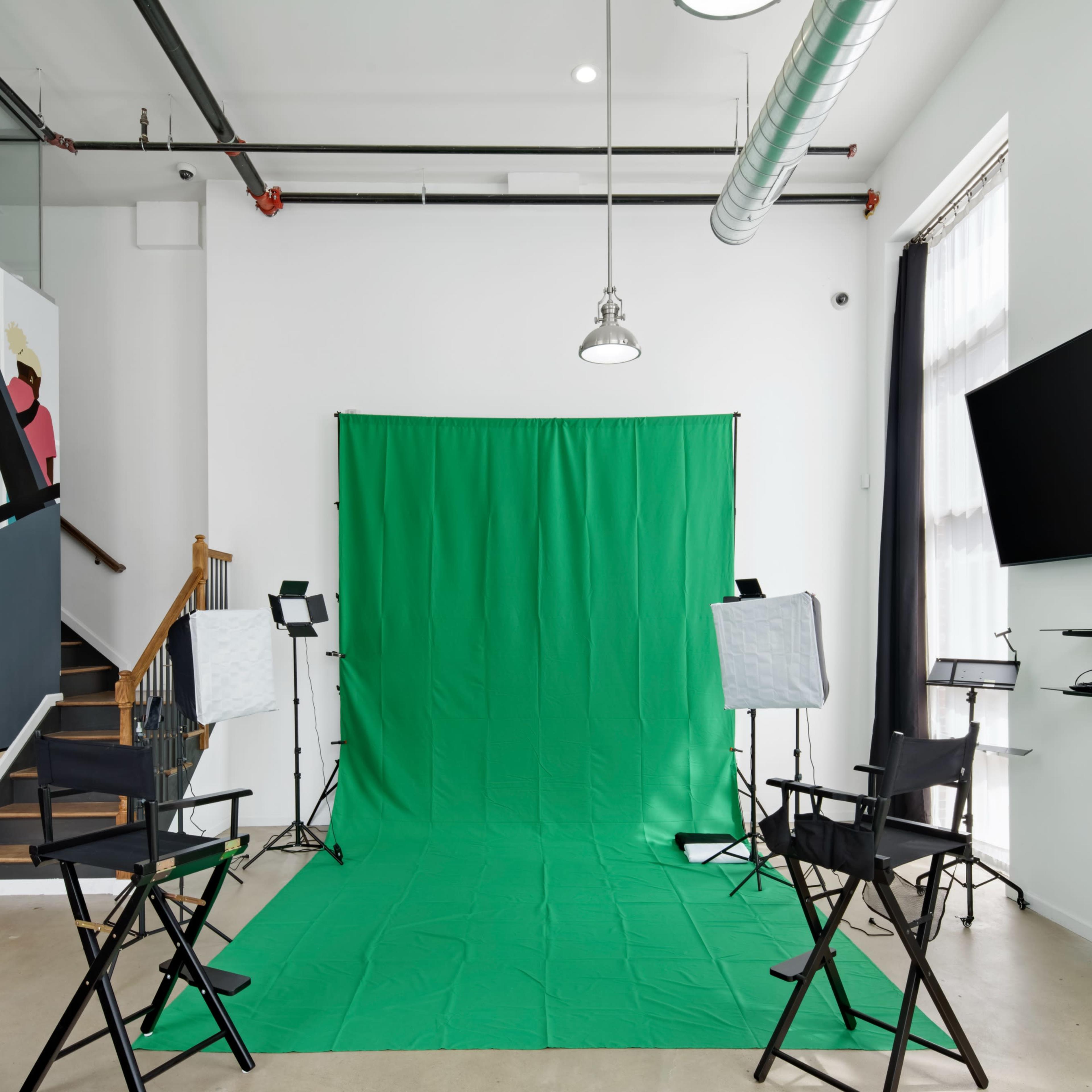 A studio space features a green screen backdrop, two lighting setups, and black director's chairs arranged in front of it.