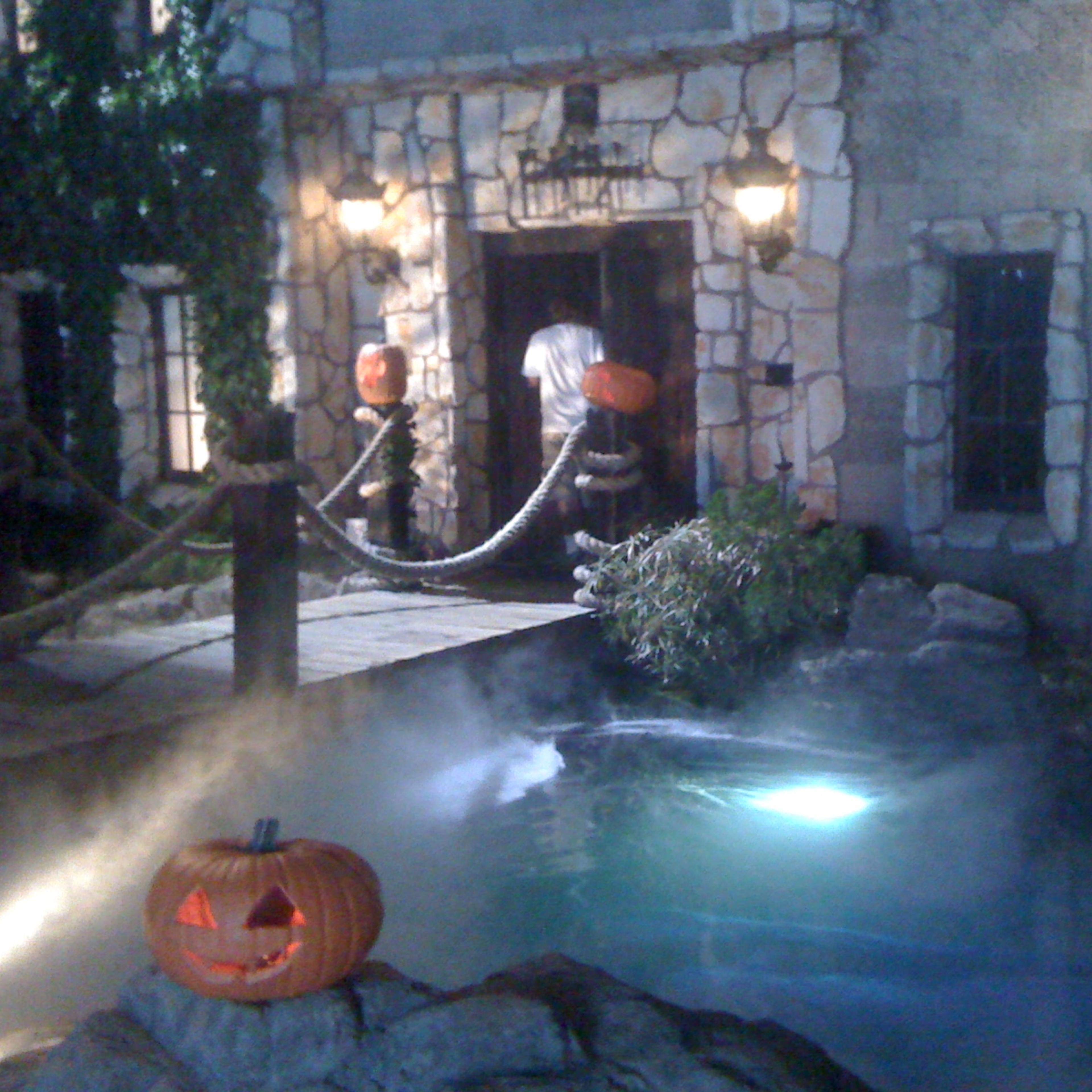 The scene depicts a foggy outdoor setting with a stone building, a pumpkin decoration, and a dimly lit pathway leading to the entrance.