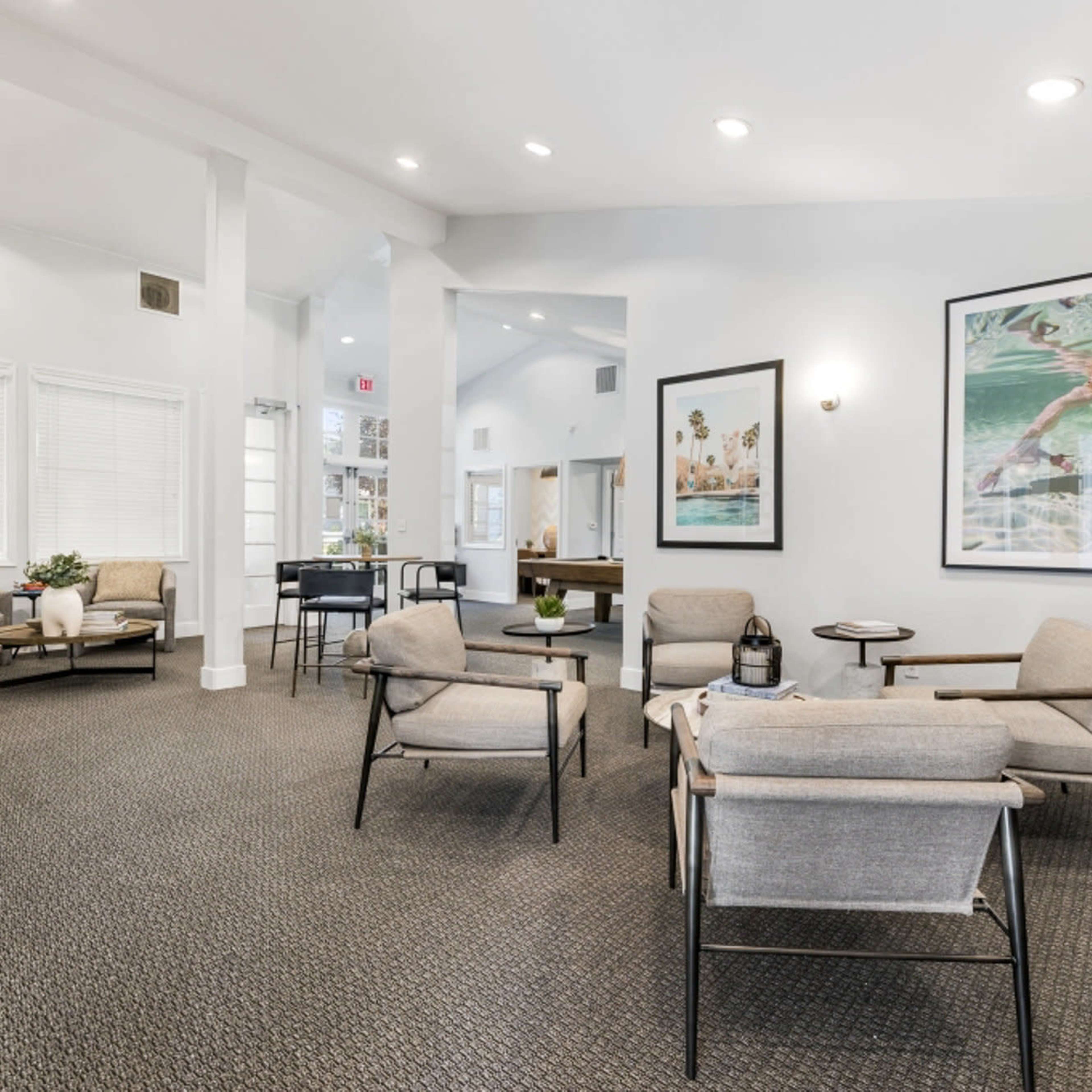 A modern common area featuring gray upholstered chairs, a wooden table, and framed artwork on the walls.