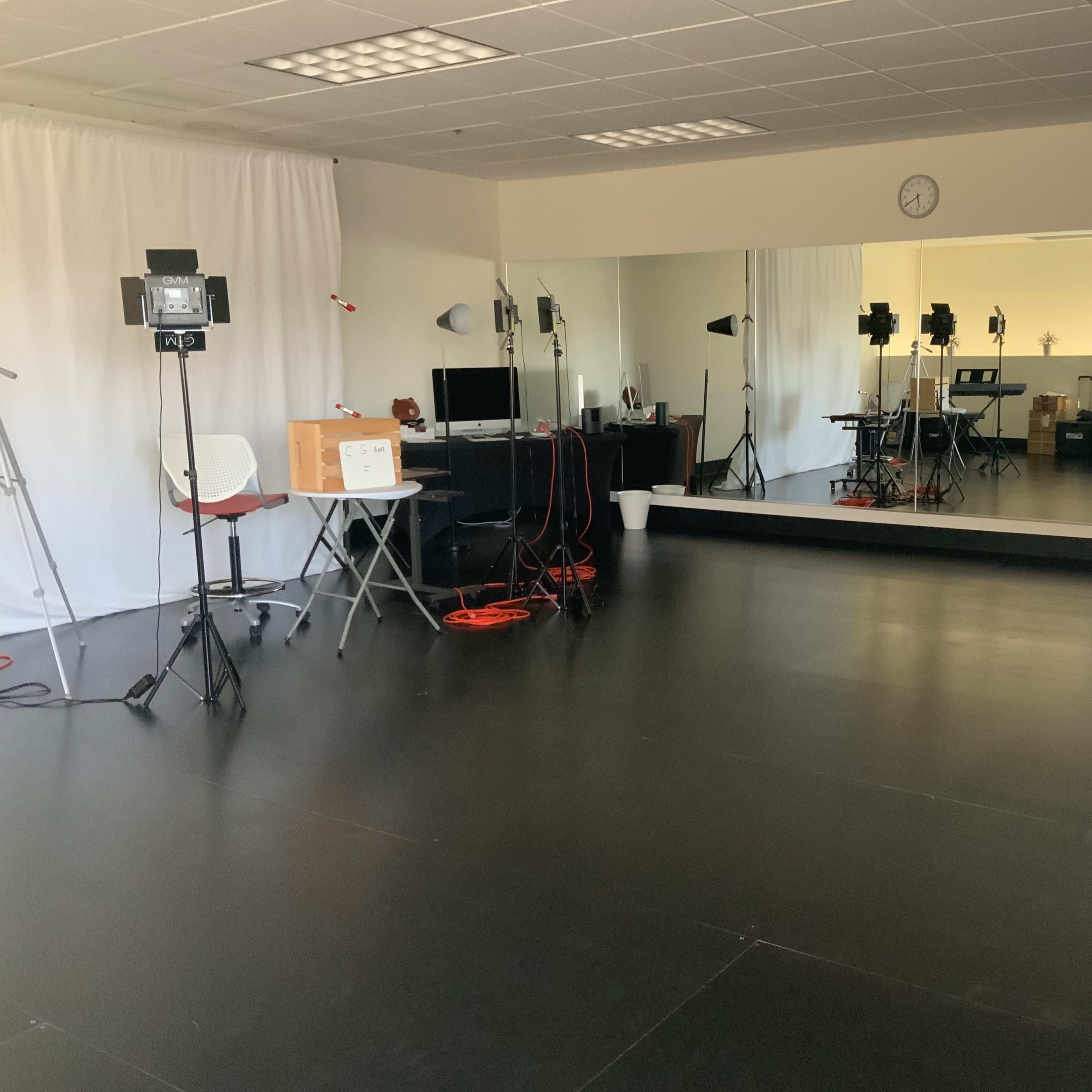 A spacious studio with black flooring, a large mirror, and various filming equipment set up, including lights and cameras.