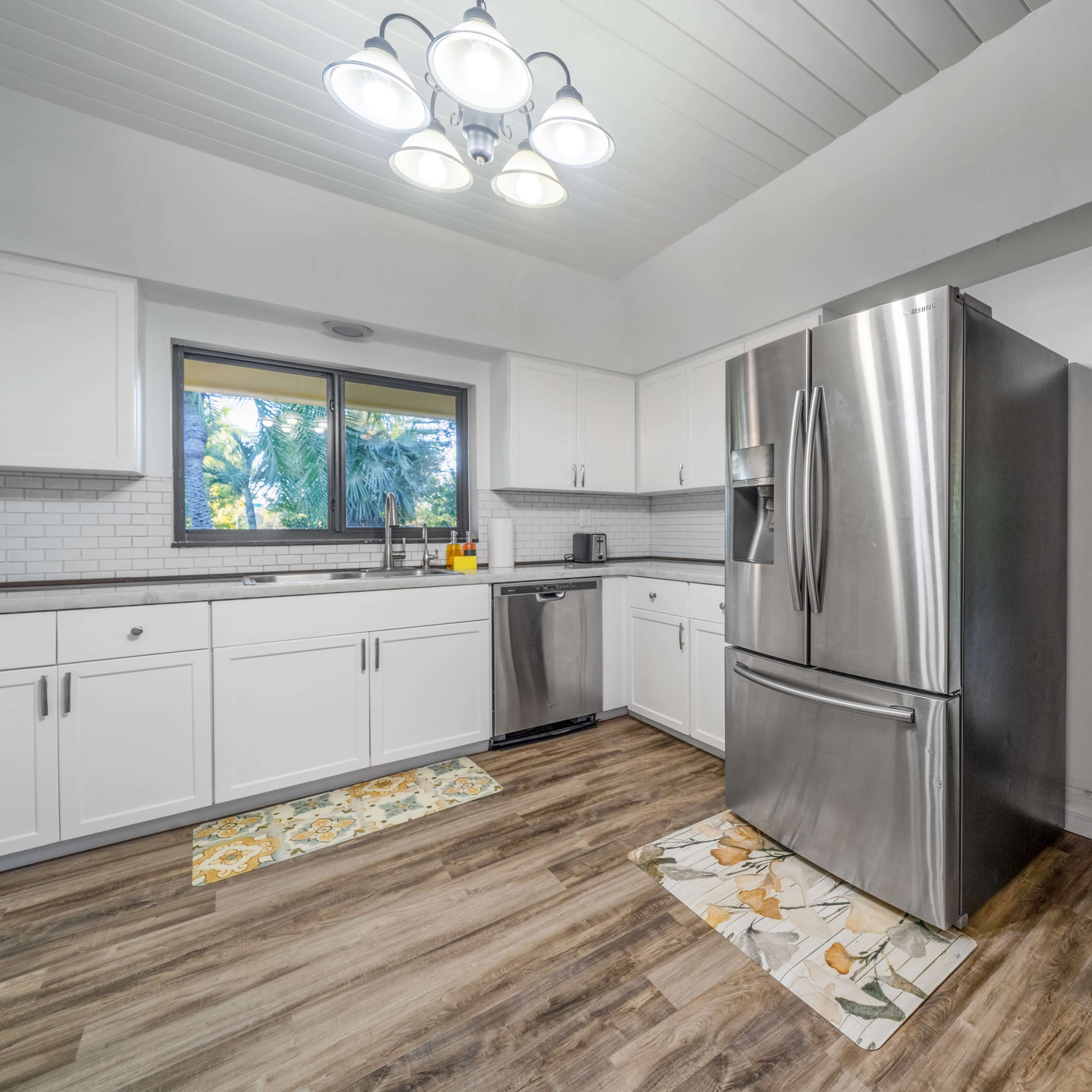 A modern kitchen features white cabinets, stainless steel appliances, and a view of an outdoor patio through a sliding glass door.