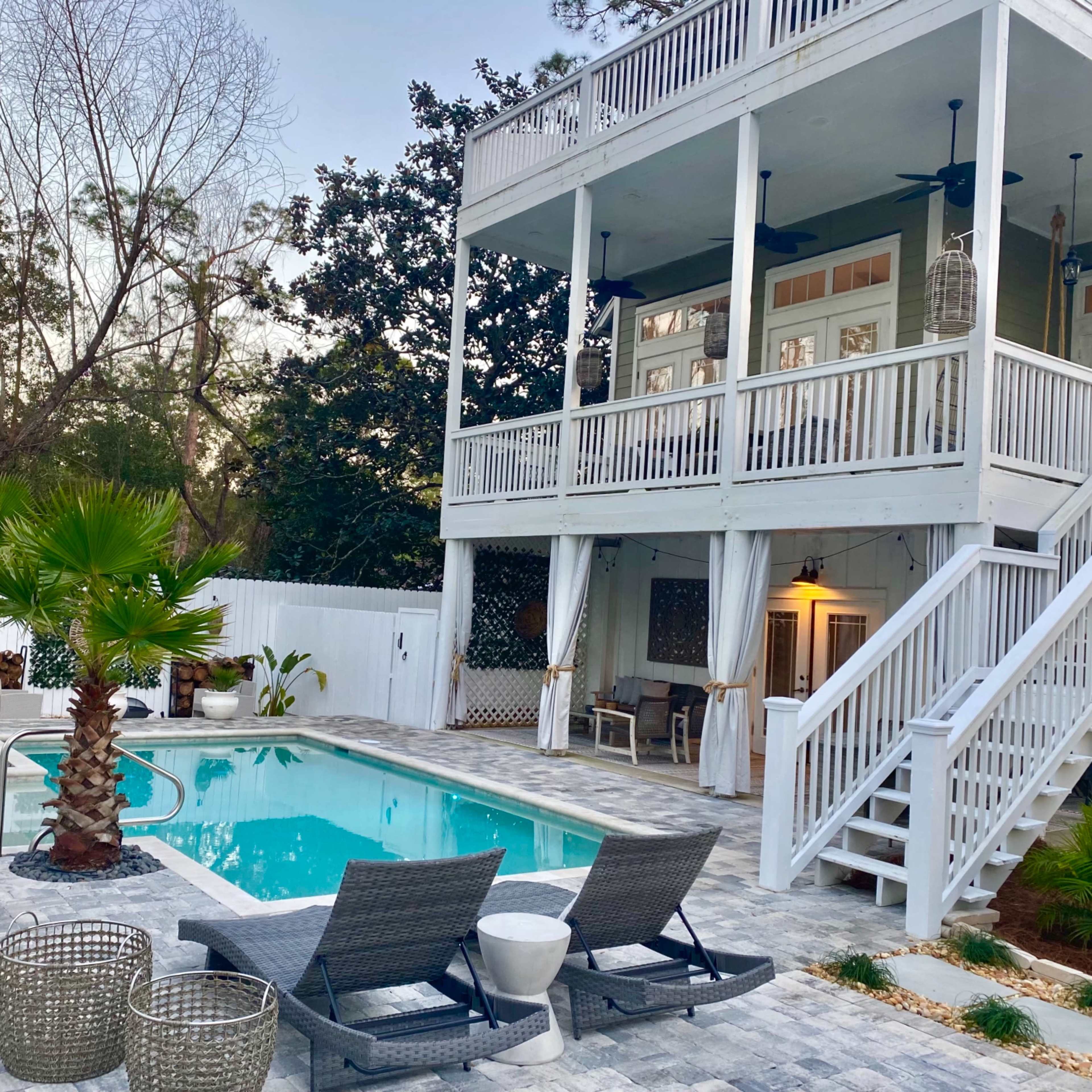 The scene features a two-story house with a private pool area surrounded by palm trees and patio furniture.