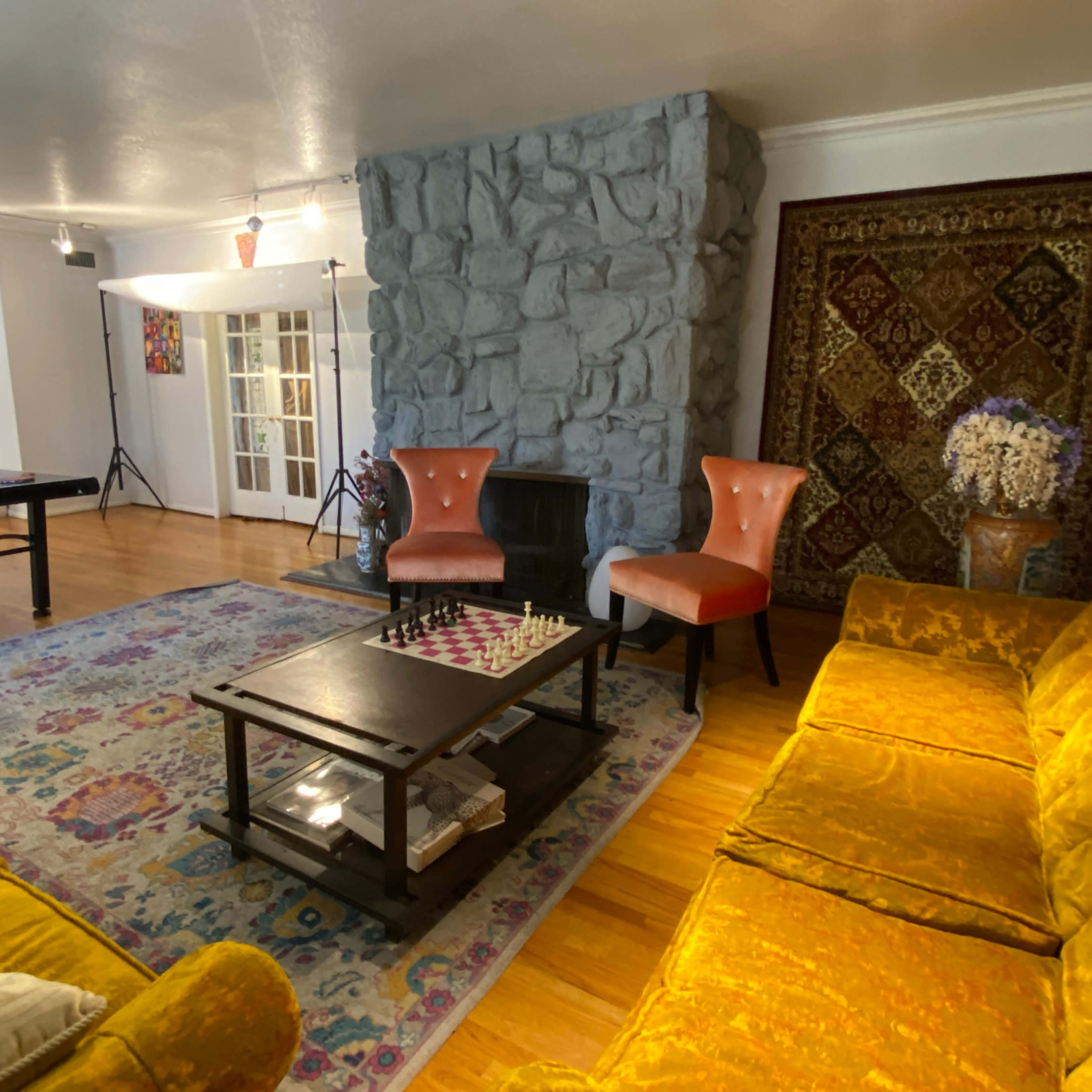 A spacious living area featuring a ping pong table, a stone fireplace, a colorful rug, and two orange armchairs flanking a coffee table with a chess set.