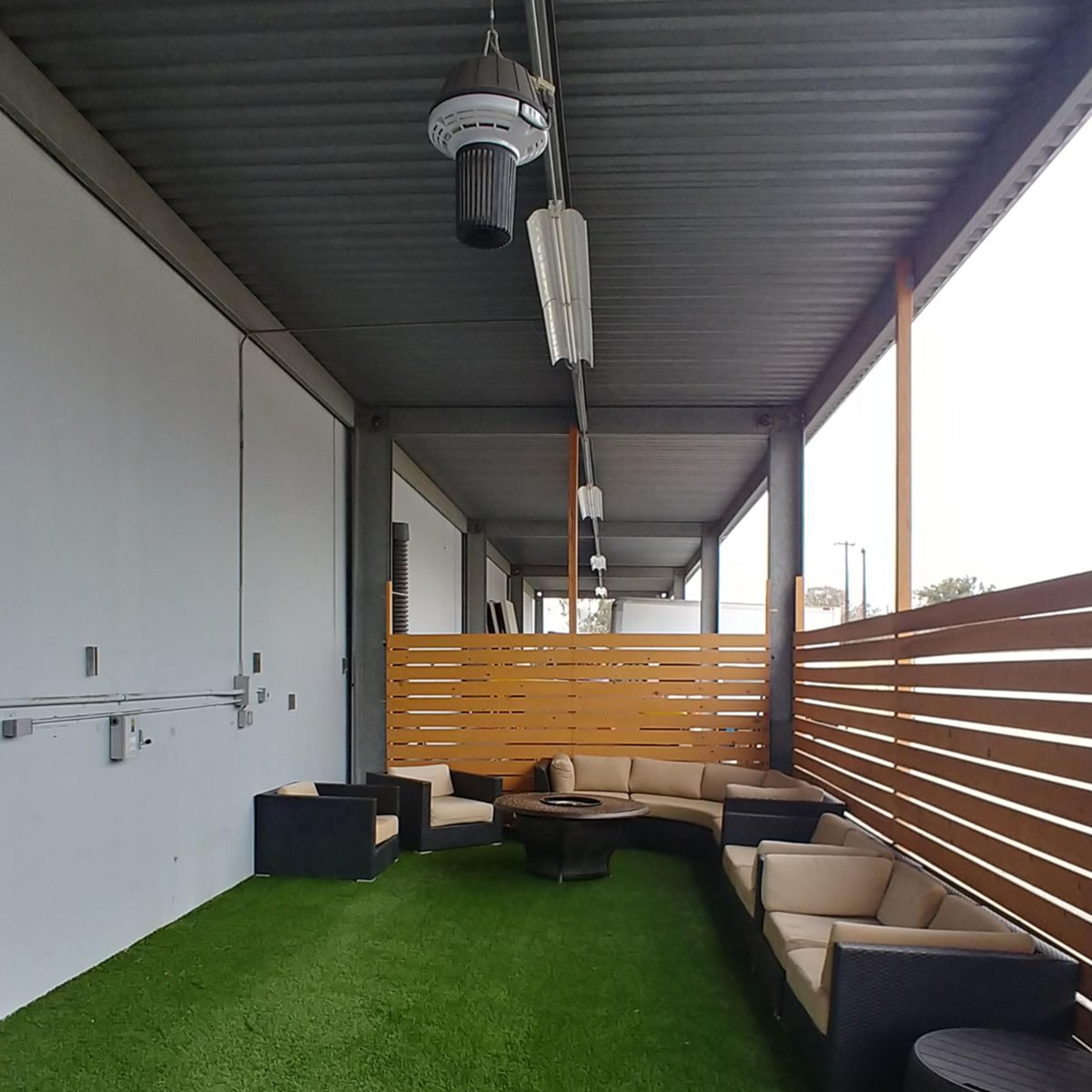 A covered outdoor area with a green artificial grass floor and a circular seating arrangement made of couches and a coffee table.