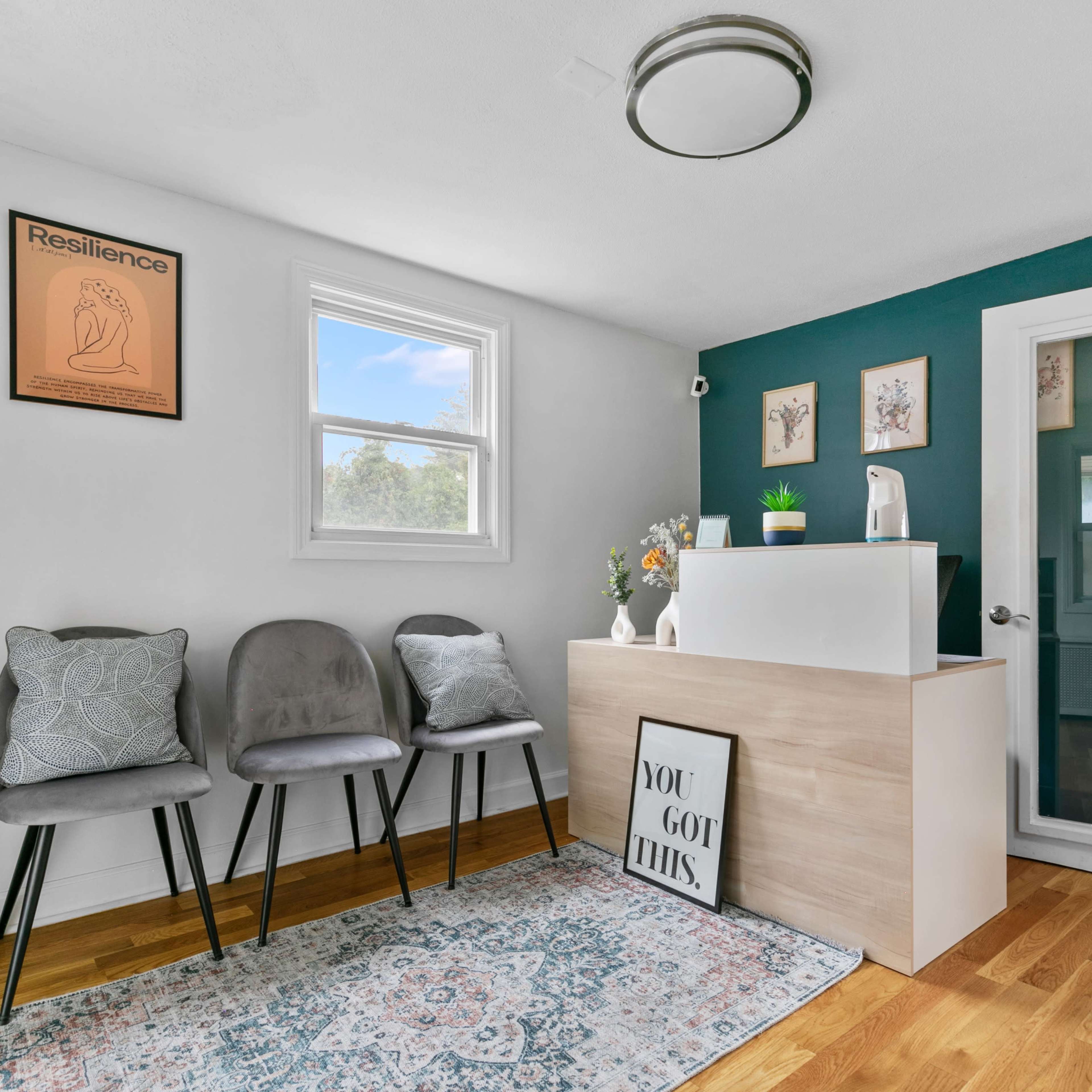 A small waiting area features a reception desk, three chairs, and decor on the walls, including framed art and a motivational poster.