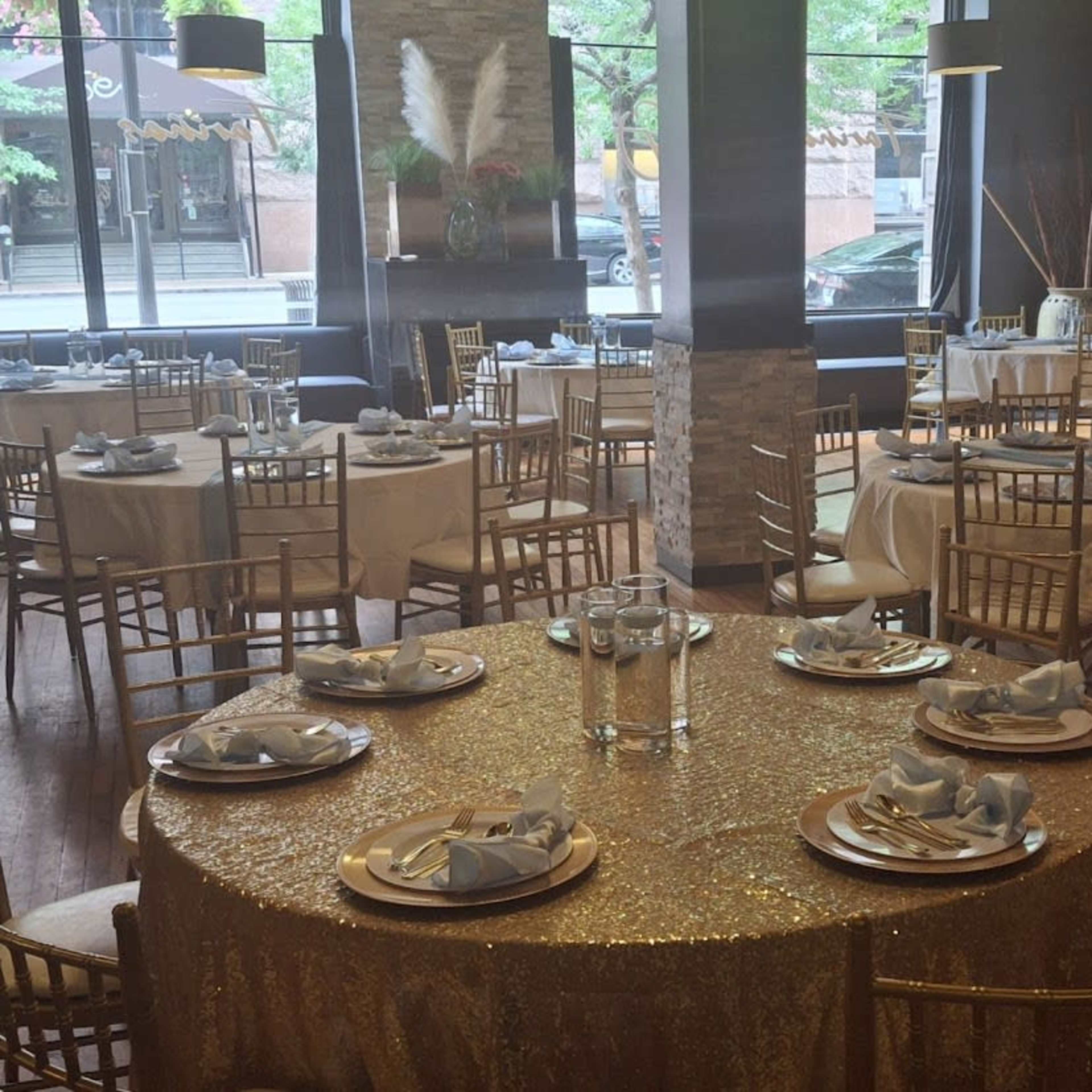 A dining area with round tables set for a formal event, featuring gold tablecloths and elegant place settings.