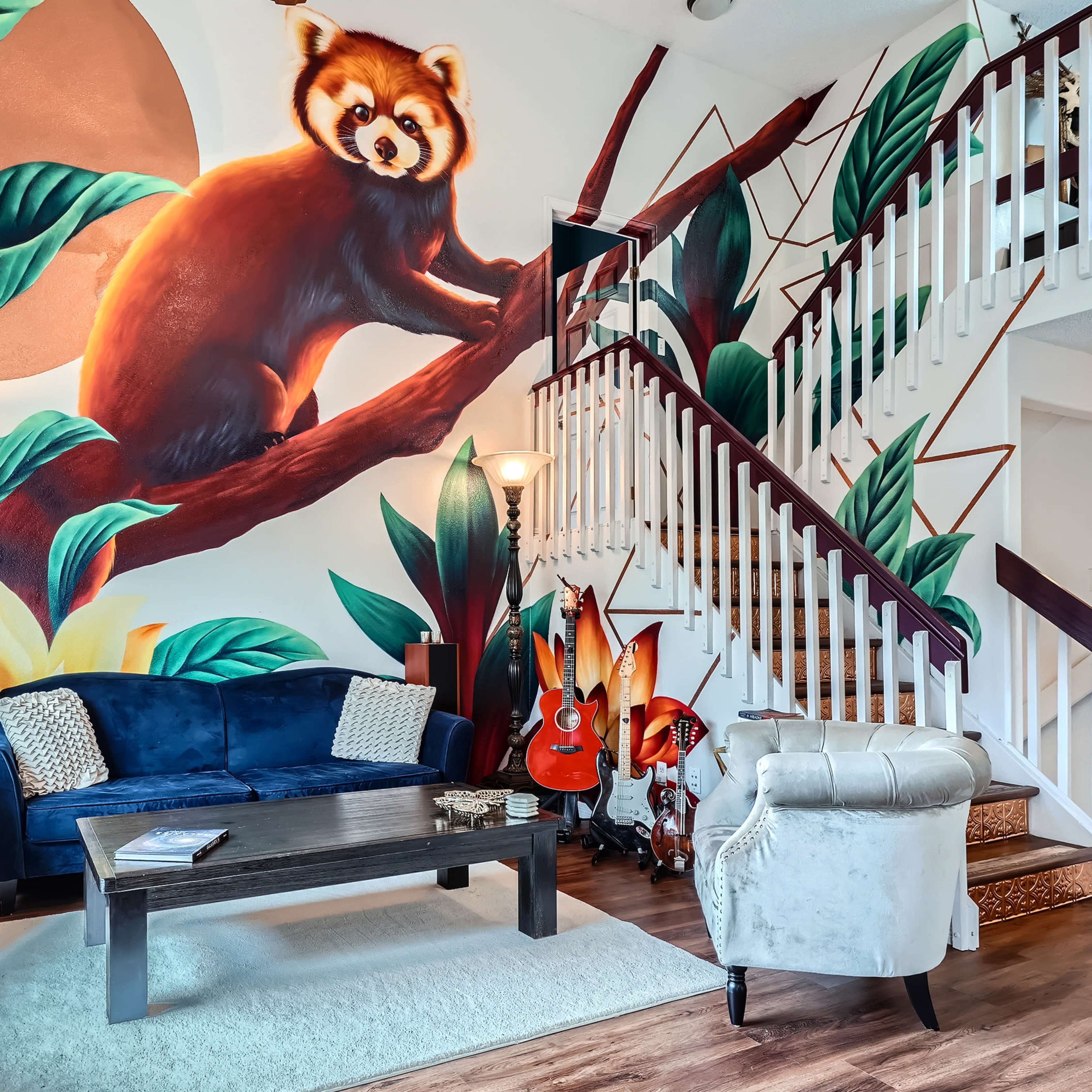A vibrant mural of a red panda adorns the wall beside a staircase in a room furnished with a blue couch and various decorative elements.