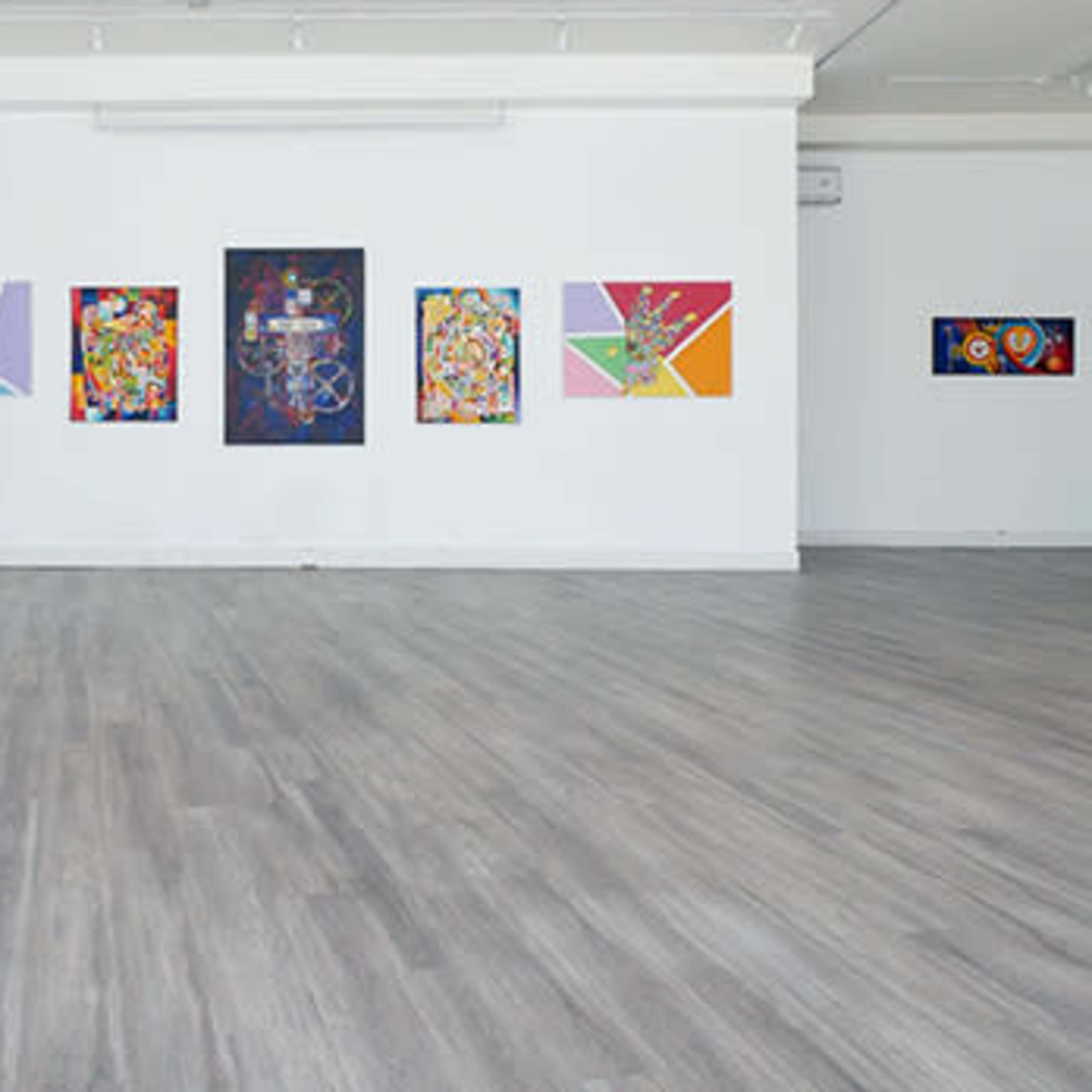 An art gallery featuring colorful paintings displayed on white walls, with a spacious wooden floor.