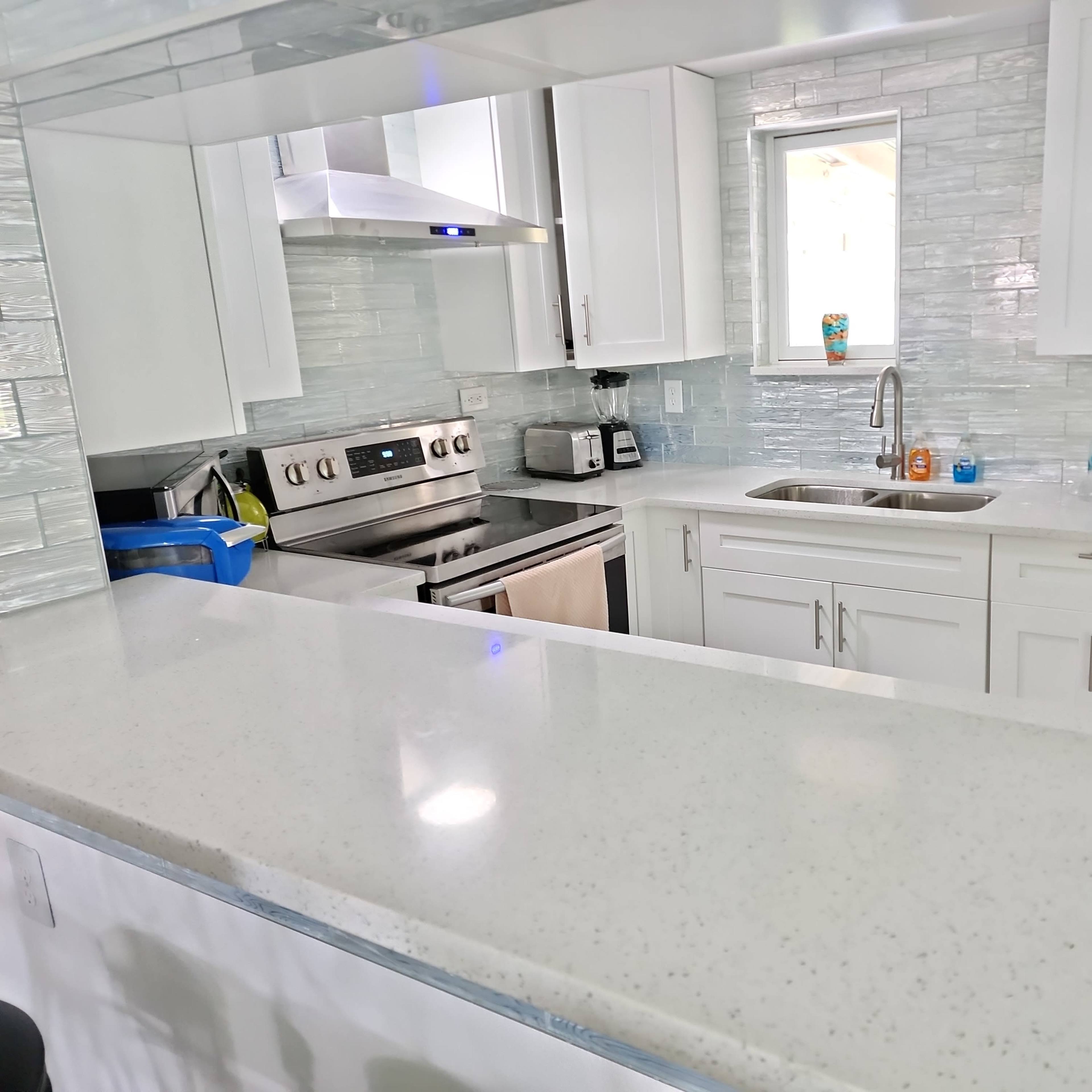 A modern kitchen with white cabinets, a stainless steel stove, and a countertop made of light-colored material.