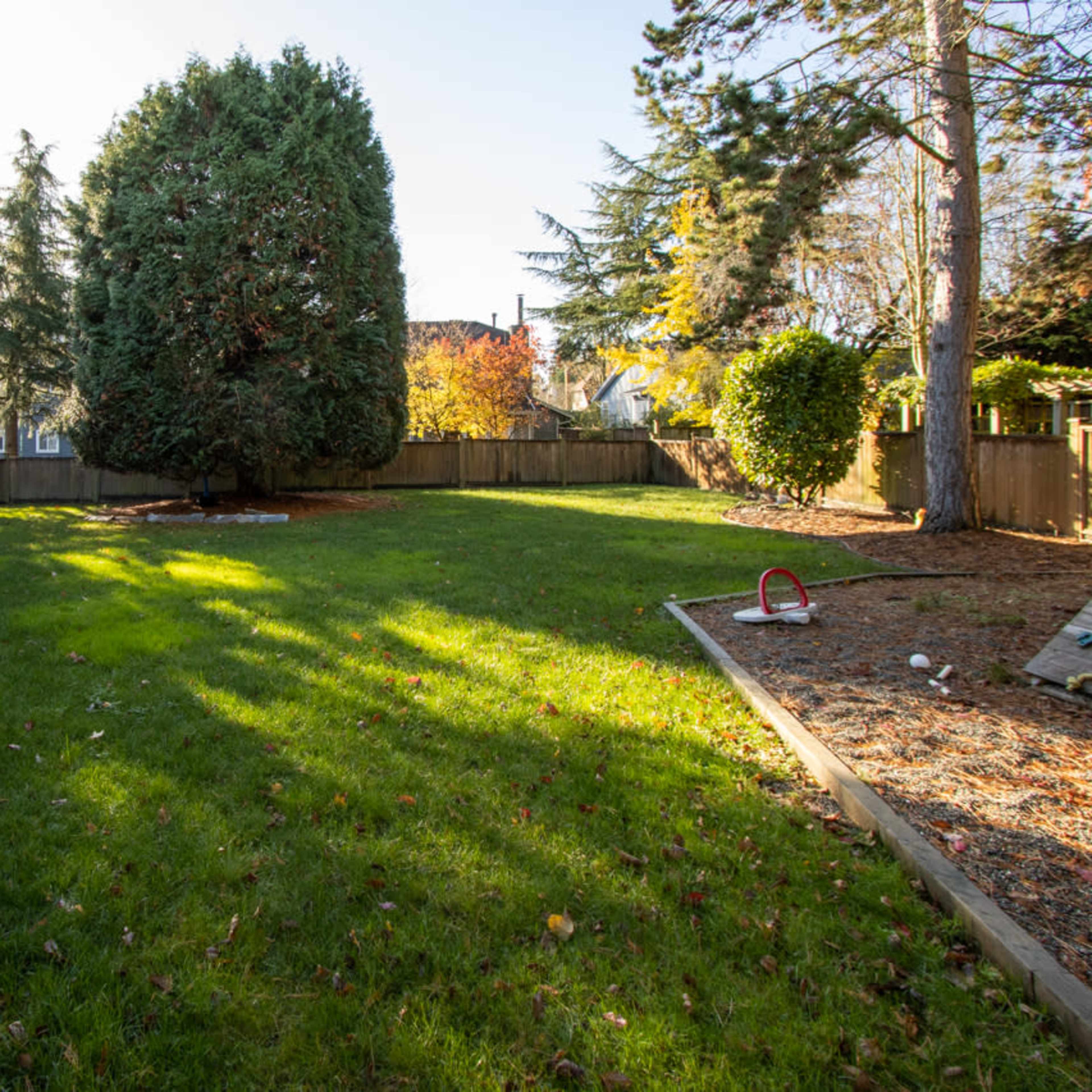 A spacious backyard features a large tree, grassy area, and a wooden deck with a railing.