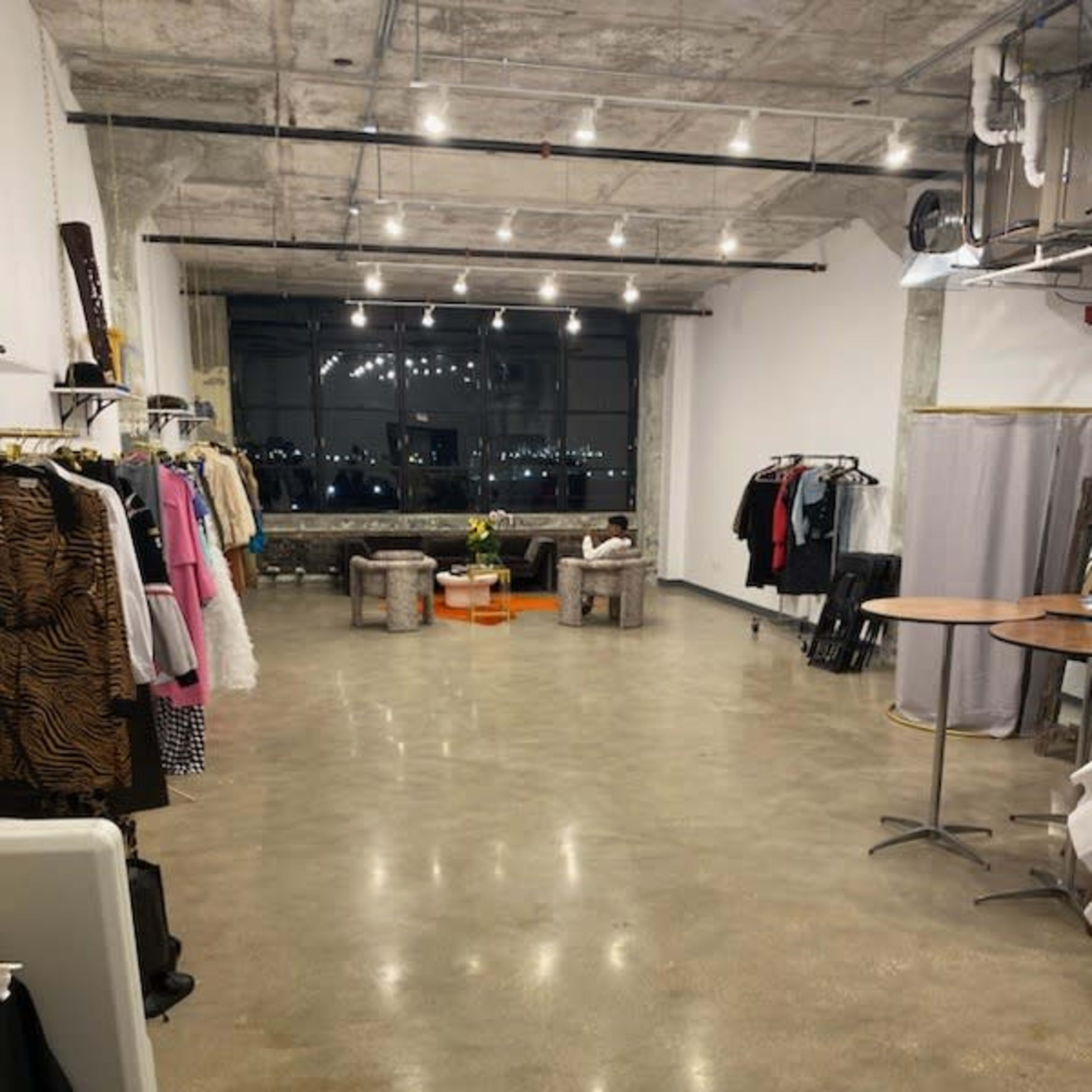 An empty, well-lit studio space with clothing racks on the sides and a seating area near a large window.