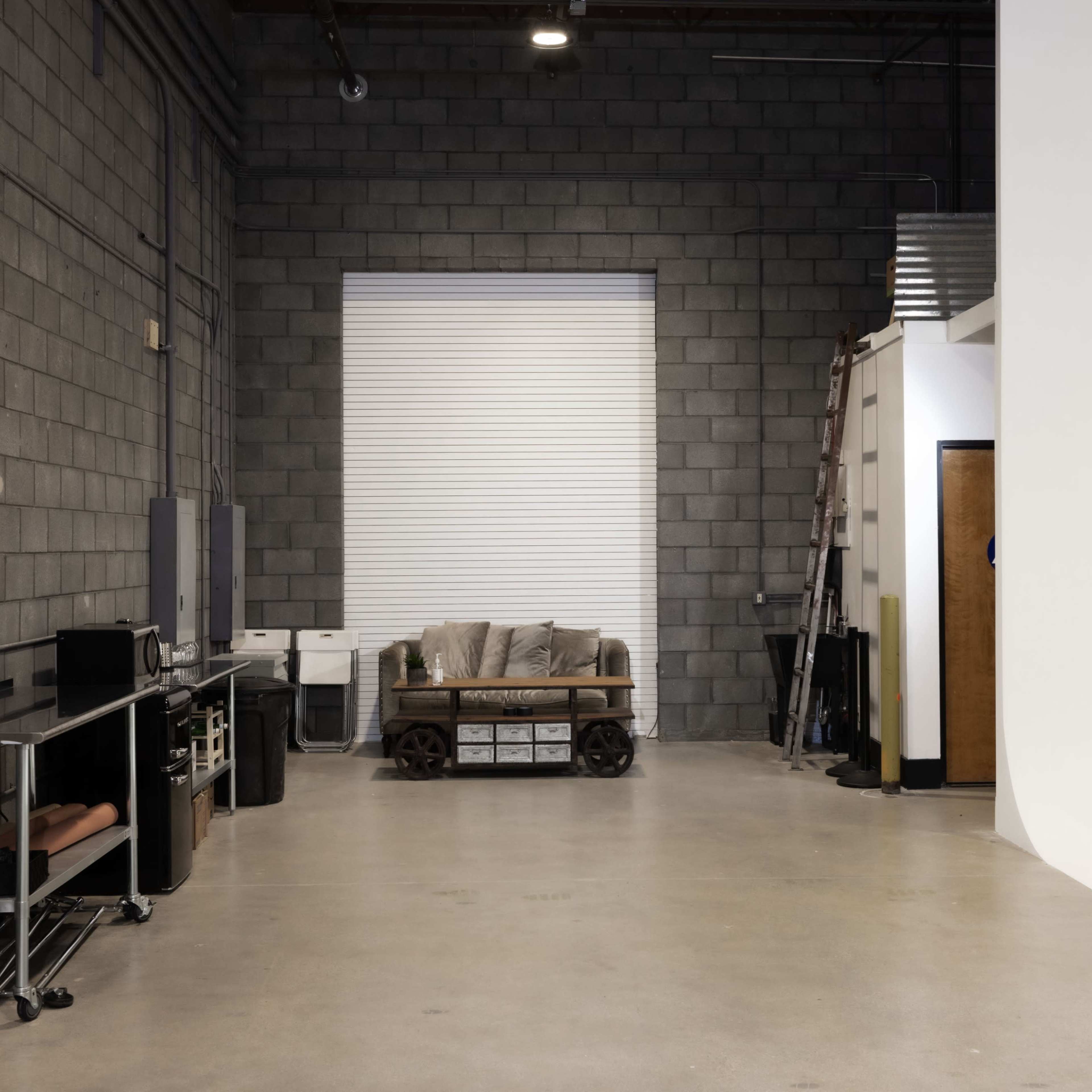 An industrial-style room with a concrete block wall, a couch on a wooden pallet, and various furniture pieces along one side.