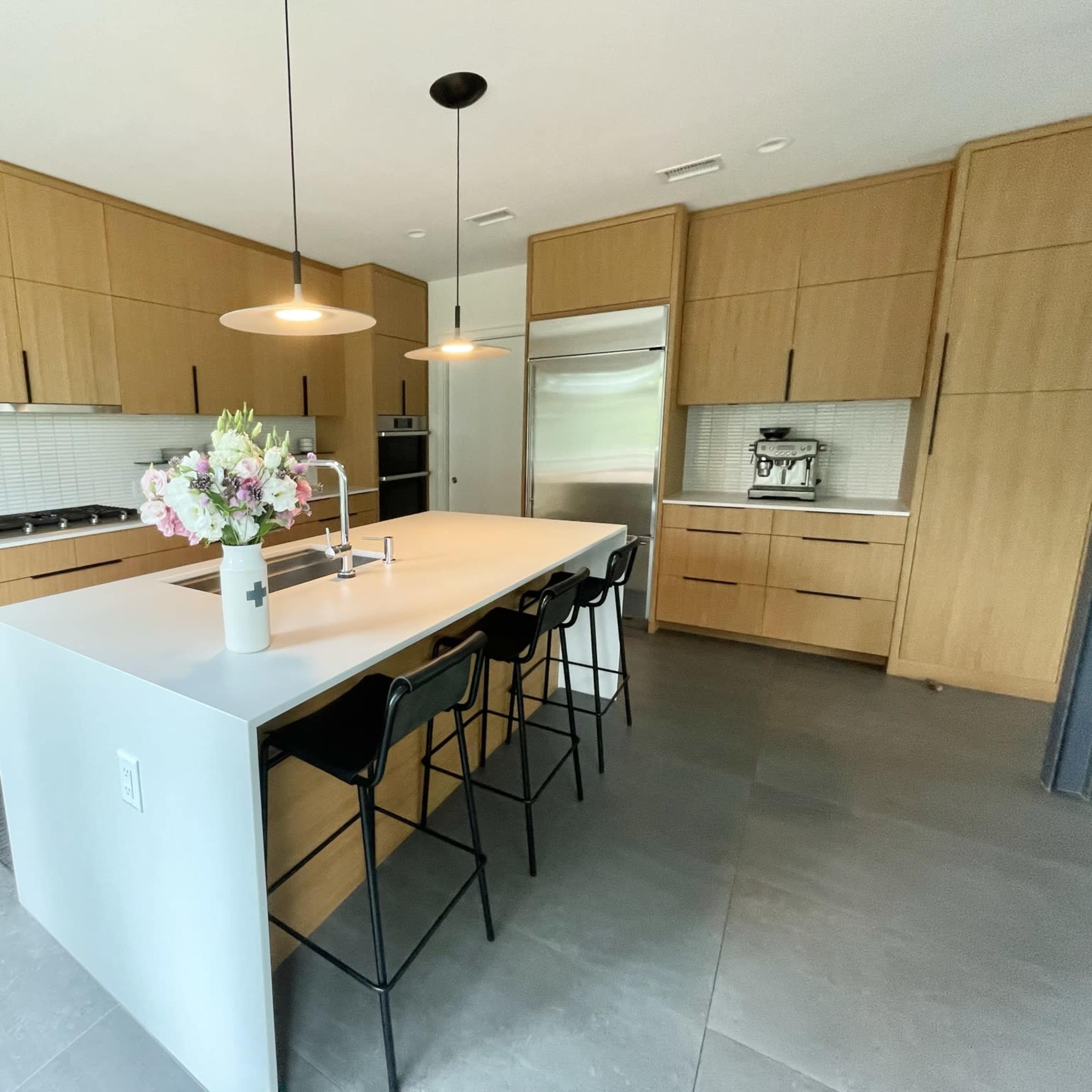 A modern kitchen features wooden cabinetry, a central island with seating, and pendant lighting above.