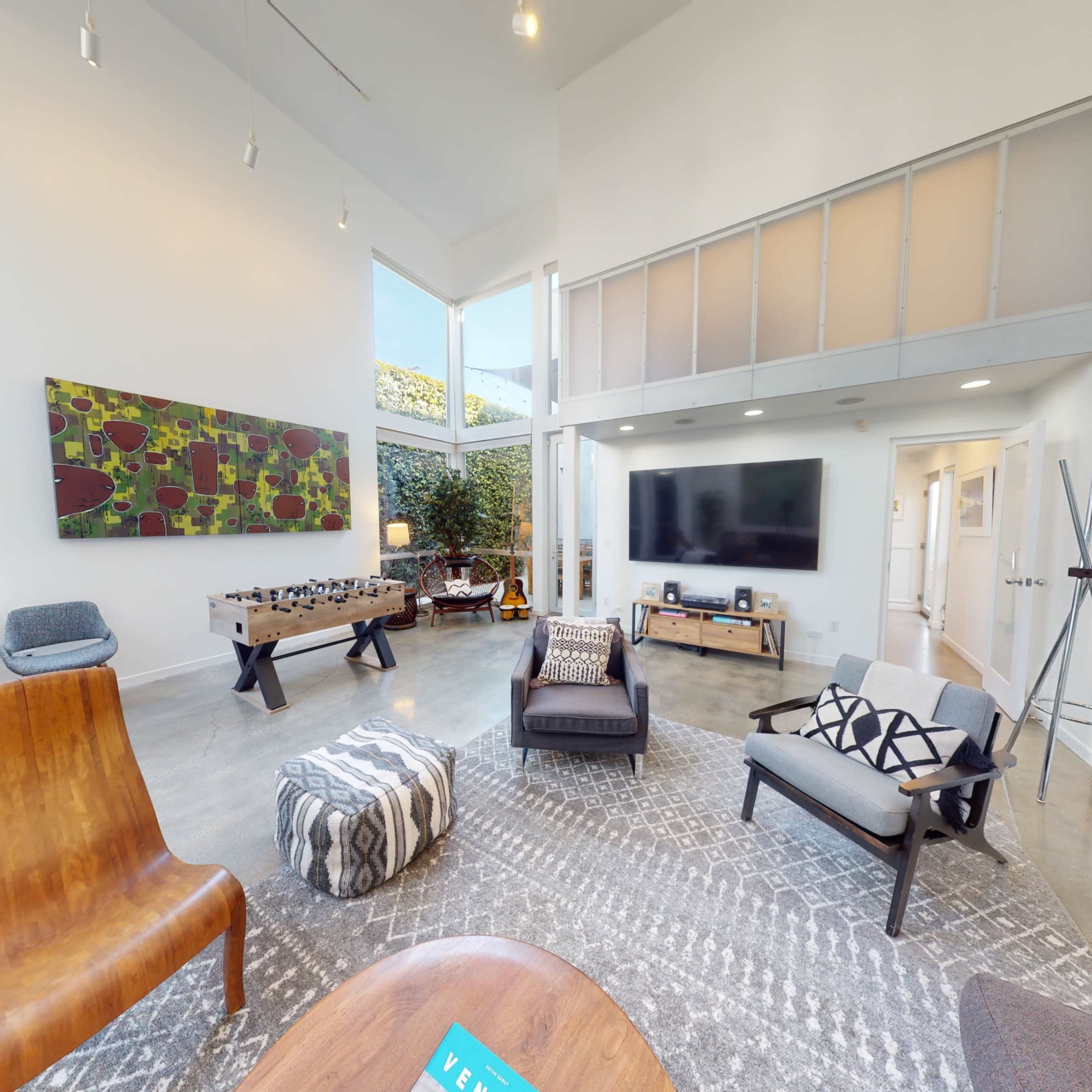 A modern, well-lit living room featuring a mix of seating options, a large television, and artistic wall decor.