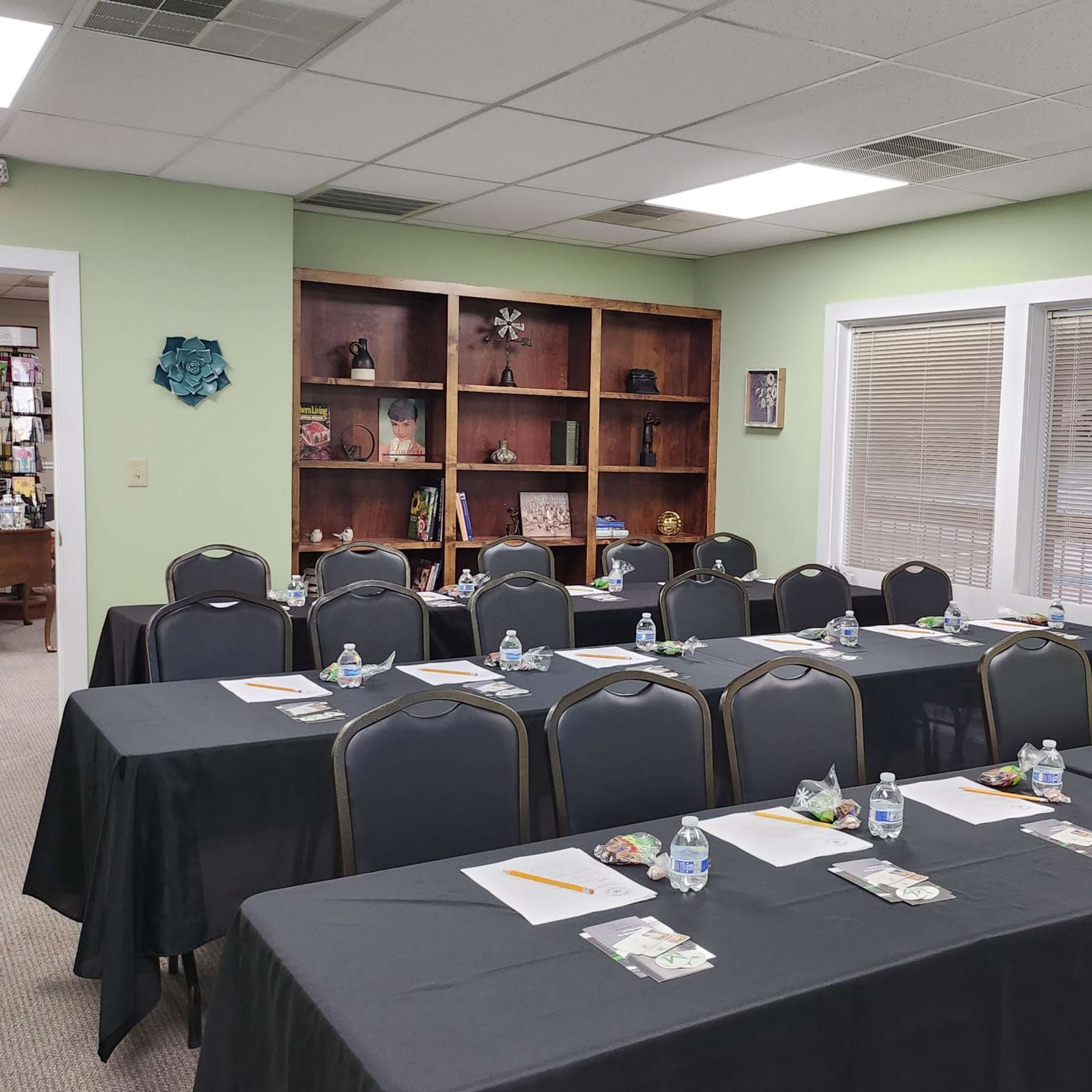 A classroom or meeting room set up with several tables covered in black cloth, each equipped with a water bottle, snacks, and writing materials.