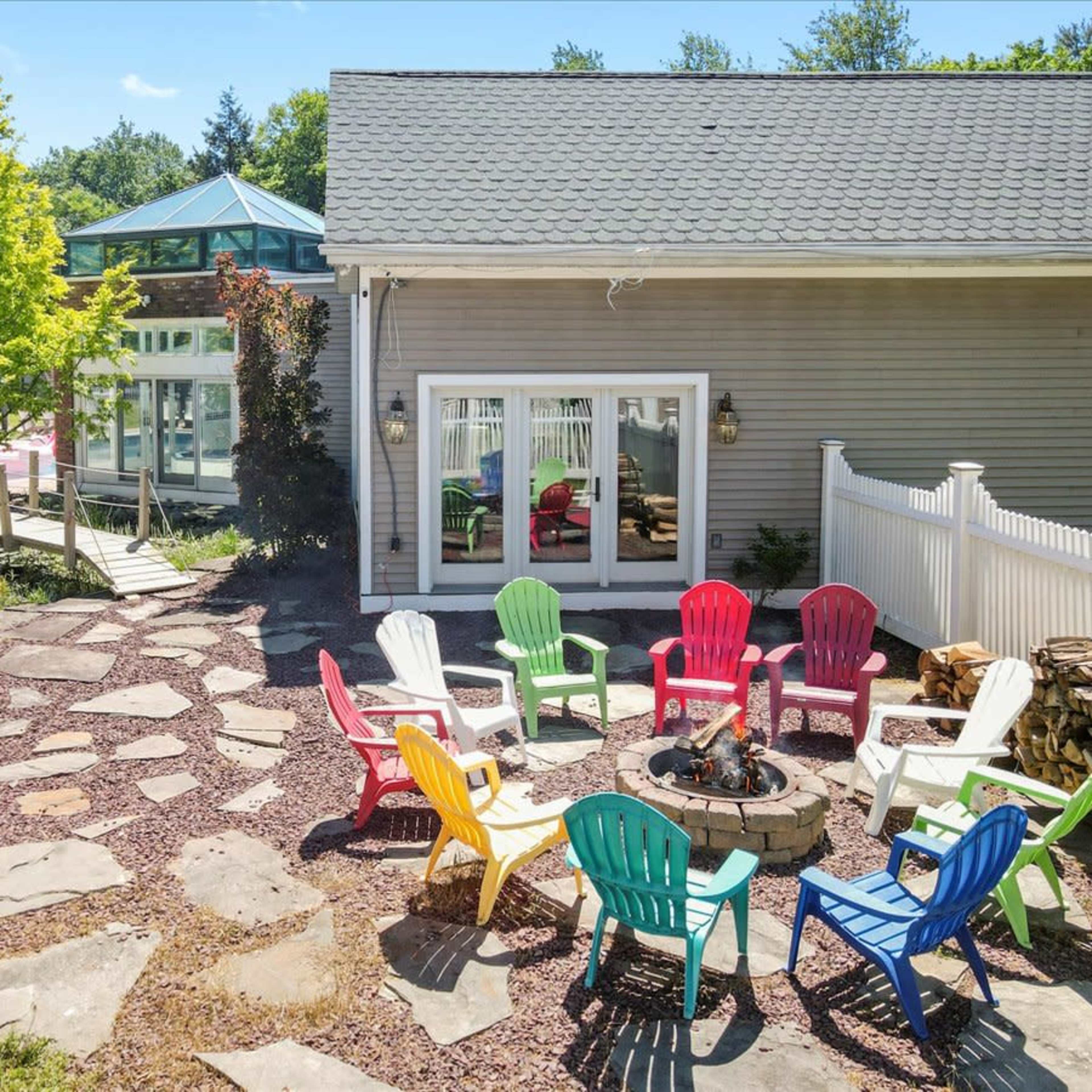 A seating area with colorful chairs surrounds a fire pit, leading to a poolside patio in a landscaped yard.