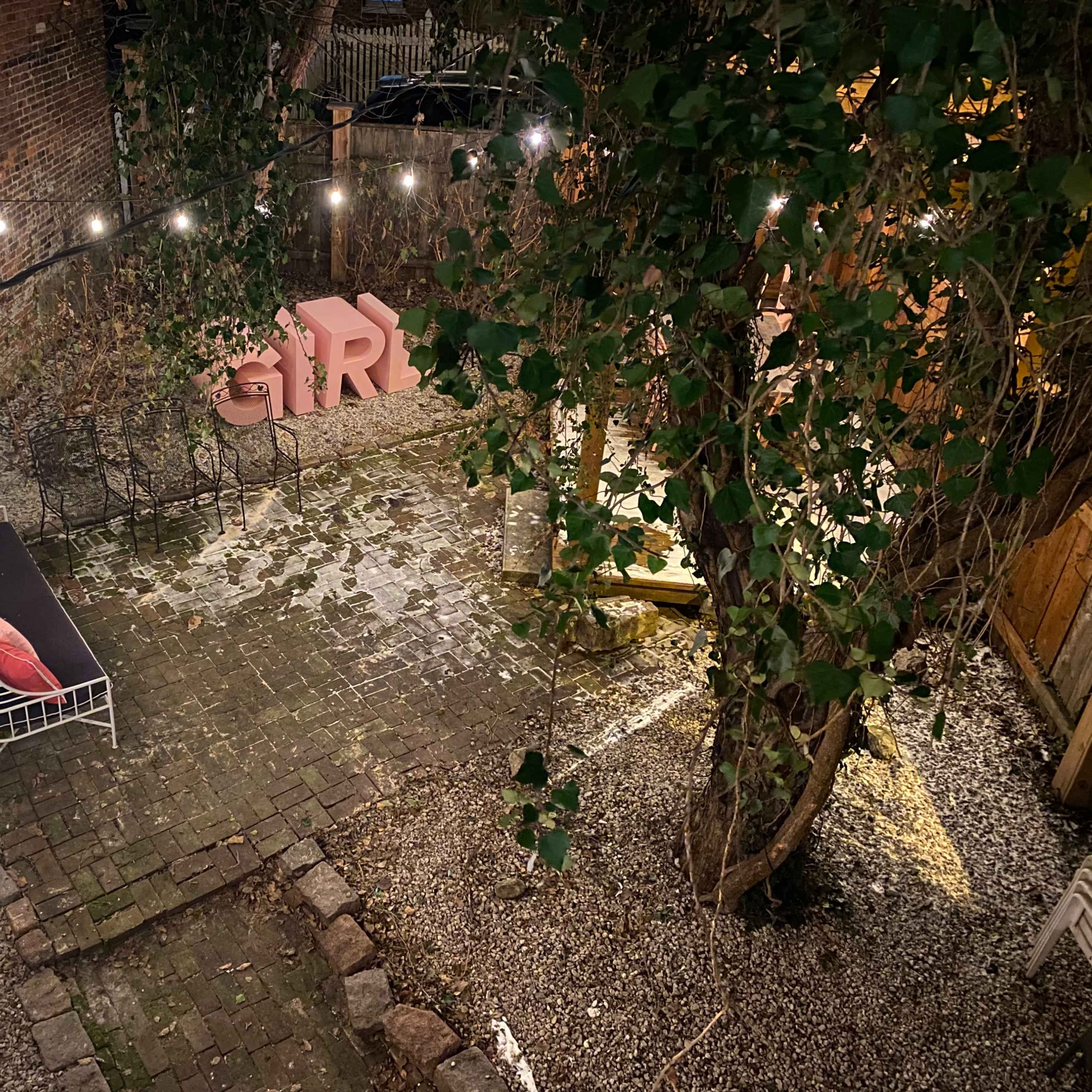 A small, outdoor garden area featuring a sofa, decorative letters, and overhead string lights among gravel and pavers.