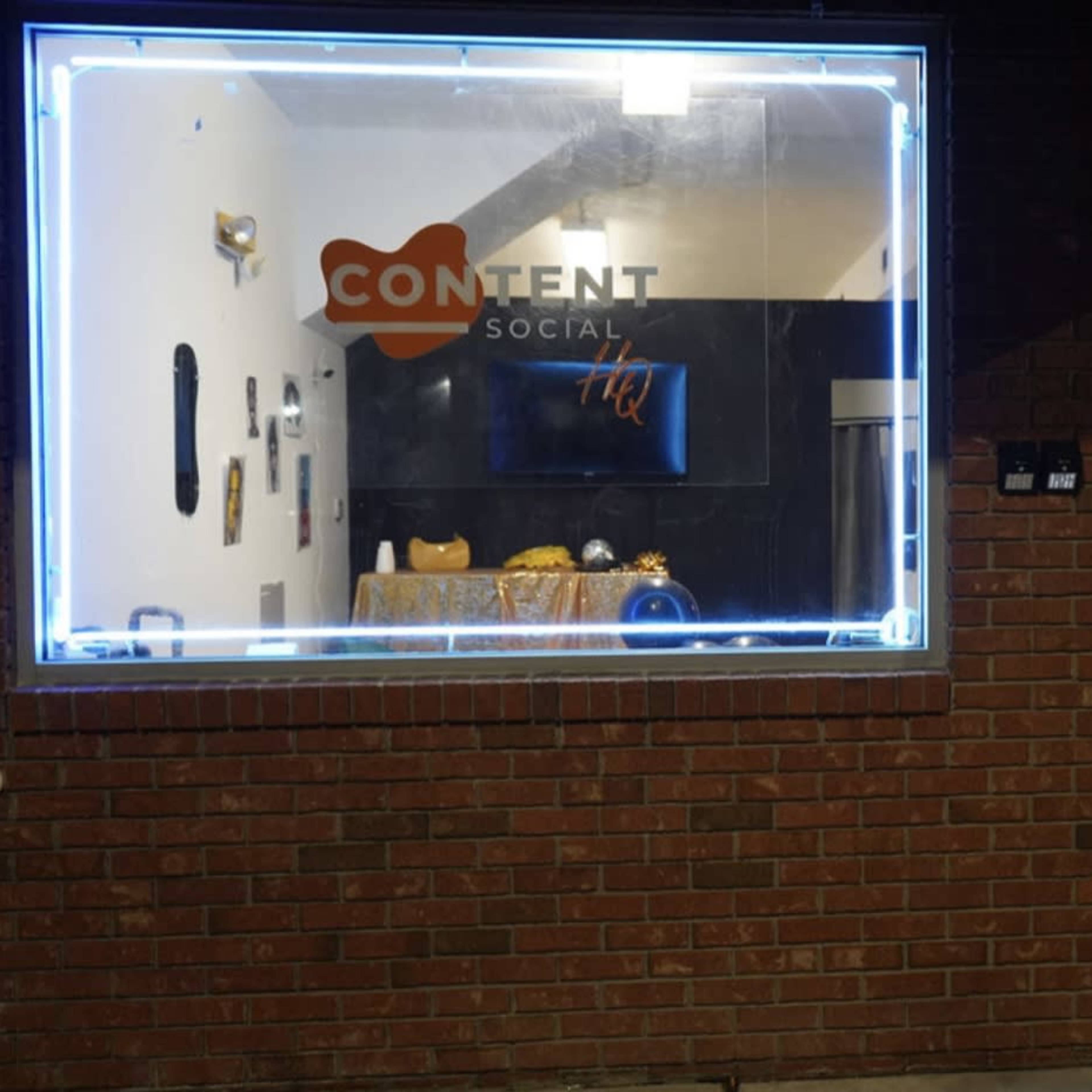 A window display of a business called "CONTENT Social" featuring a table with decorative items, next to a door with a visible address number, 2107.