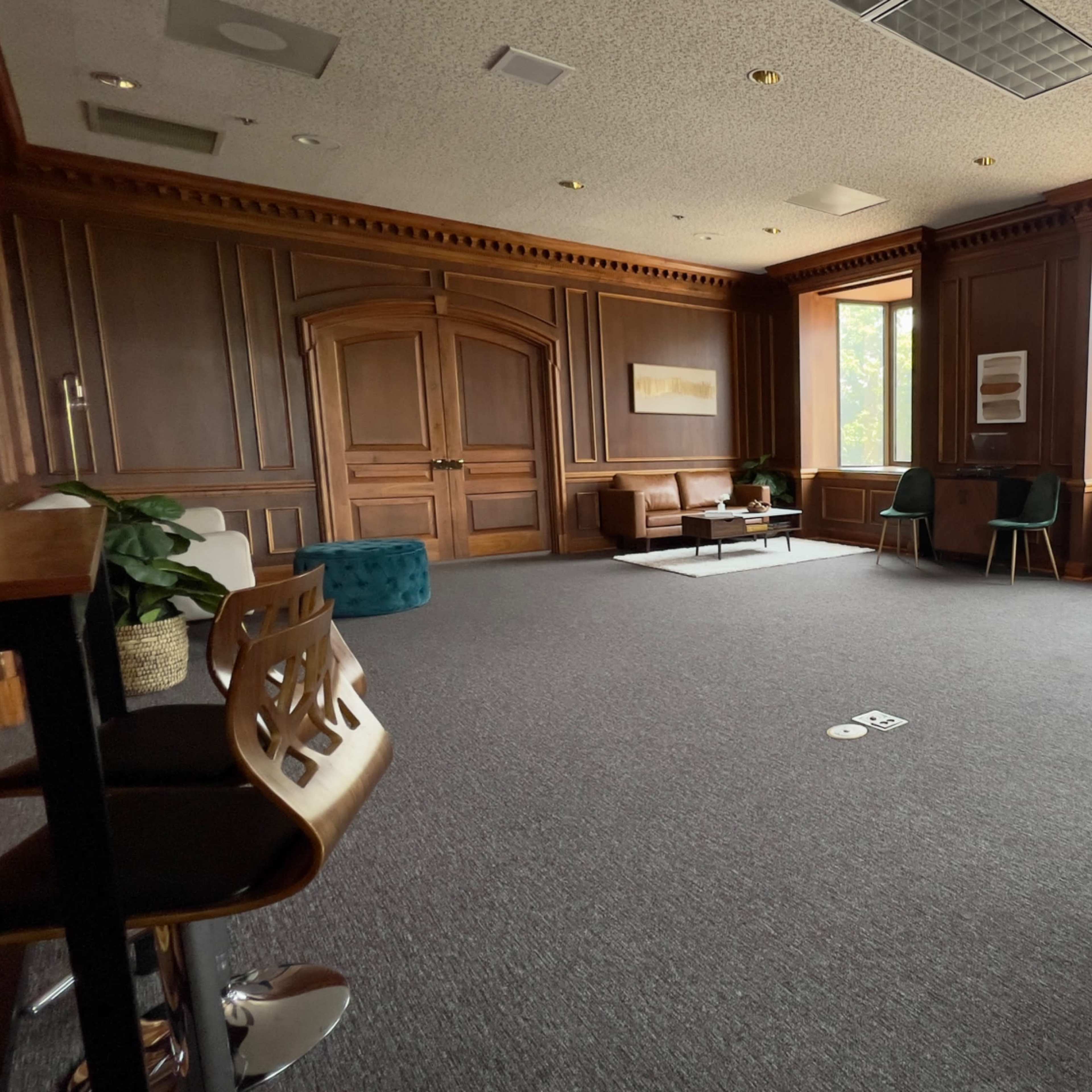 A spacious, elegantly furnished room with wooden paneling, large windows, and a mix of seating areas including chairs and a couch.