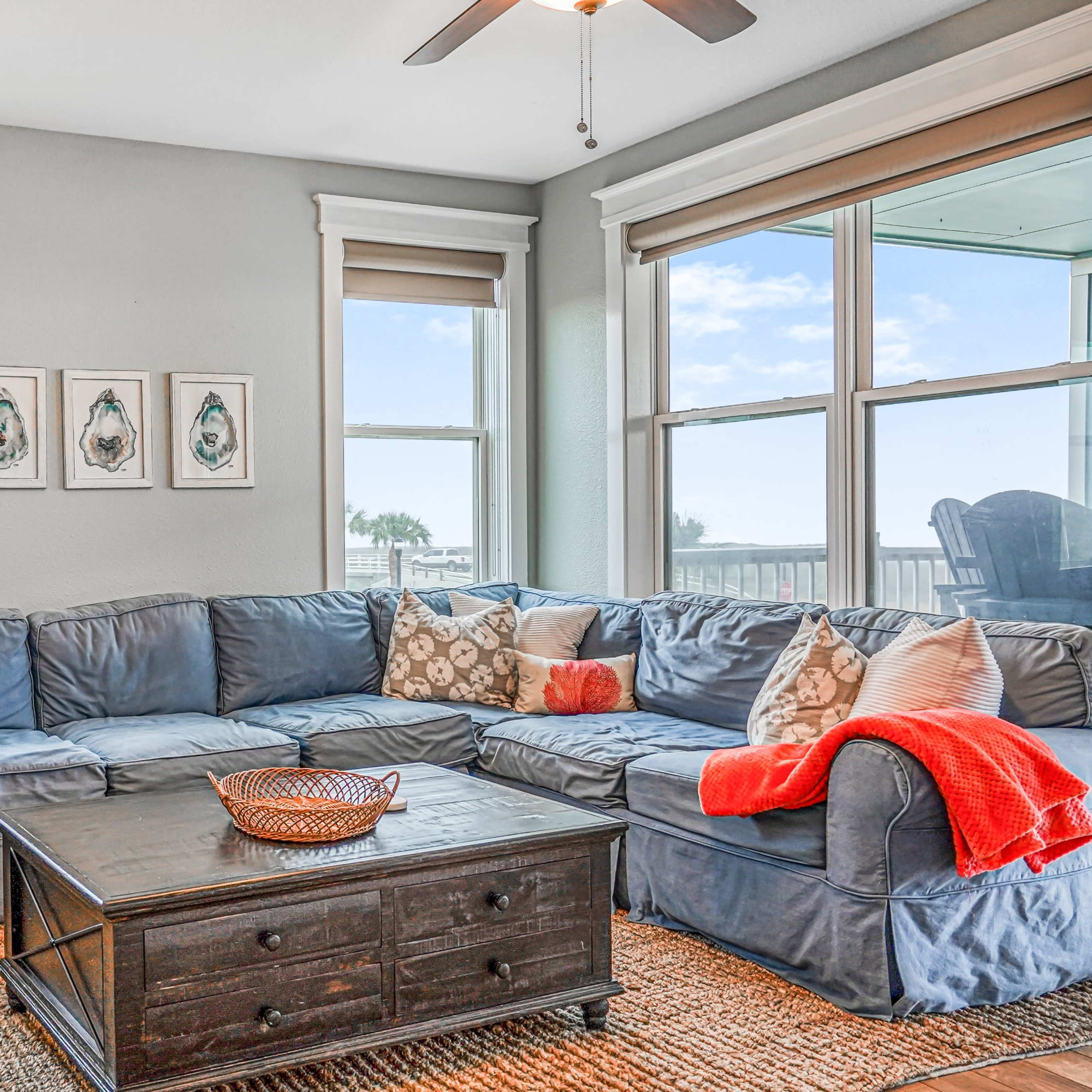 A cozy living room features a large sectional sofa with decorative pillows, a wooden coffee table, and windows that provide natural light.
