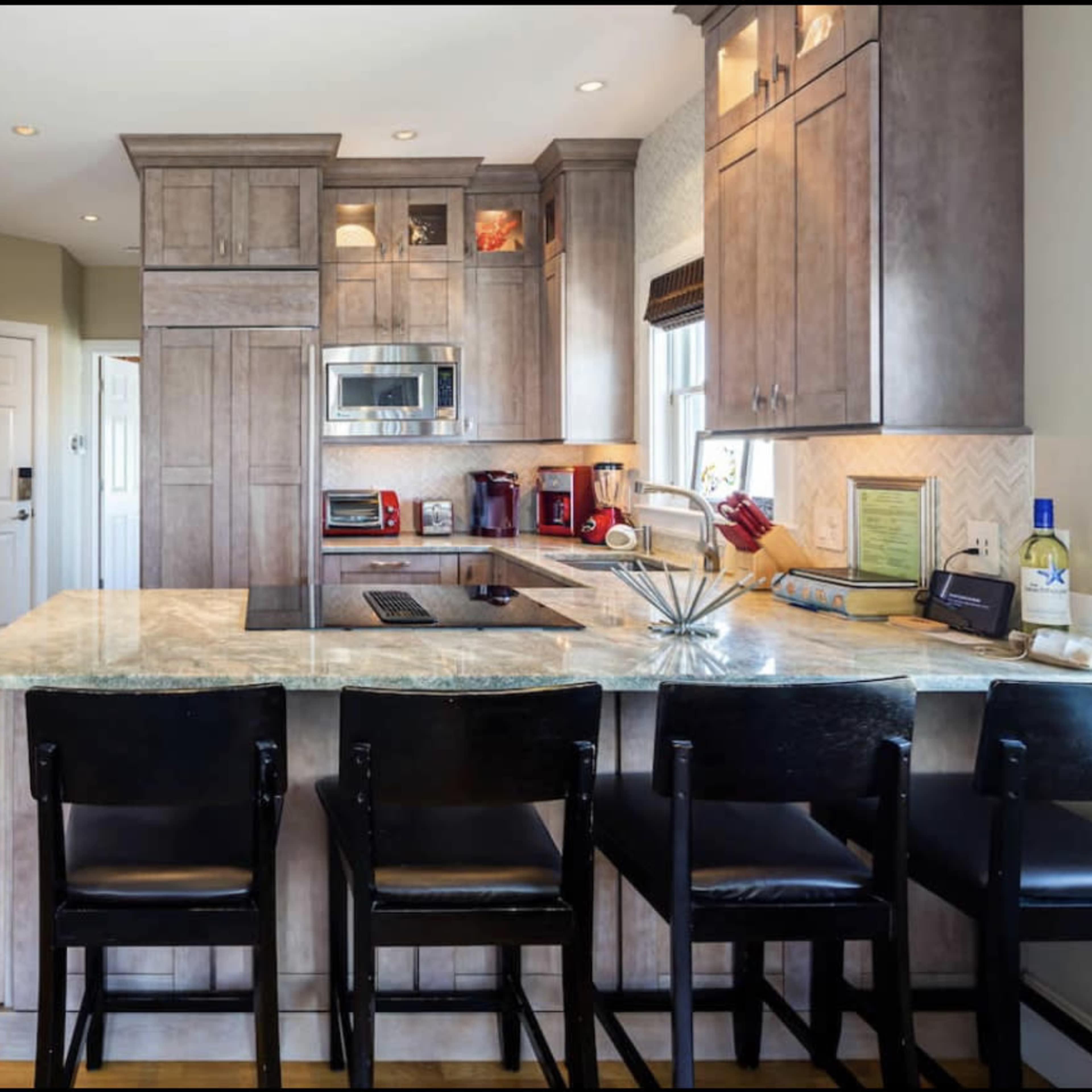 A modern kitchen featuring an island with black bar stools, wooden cabinetry, and stainless steel appliances.