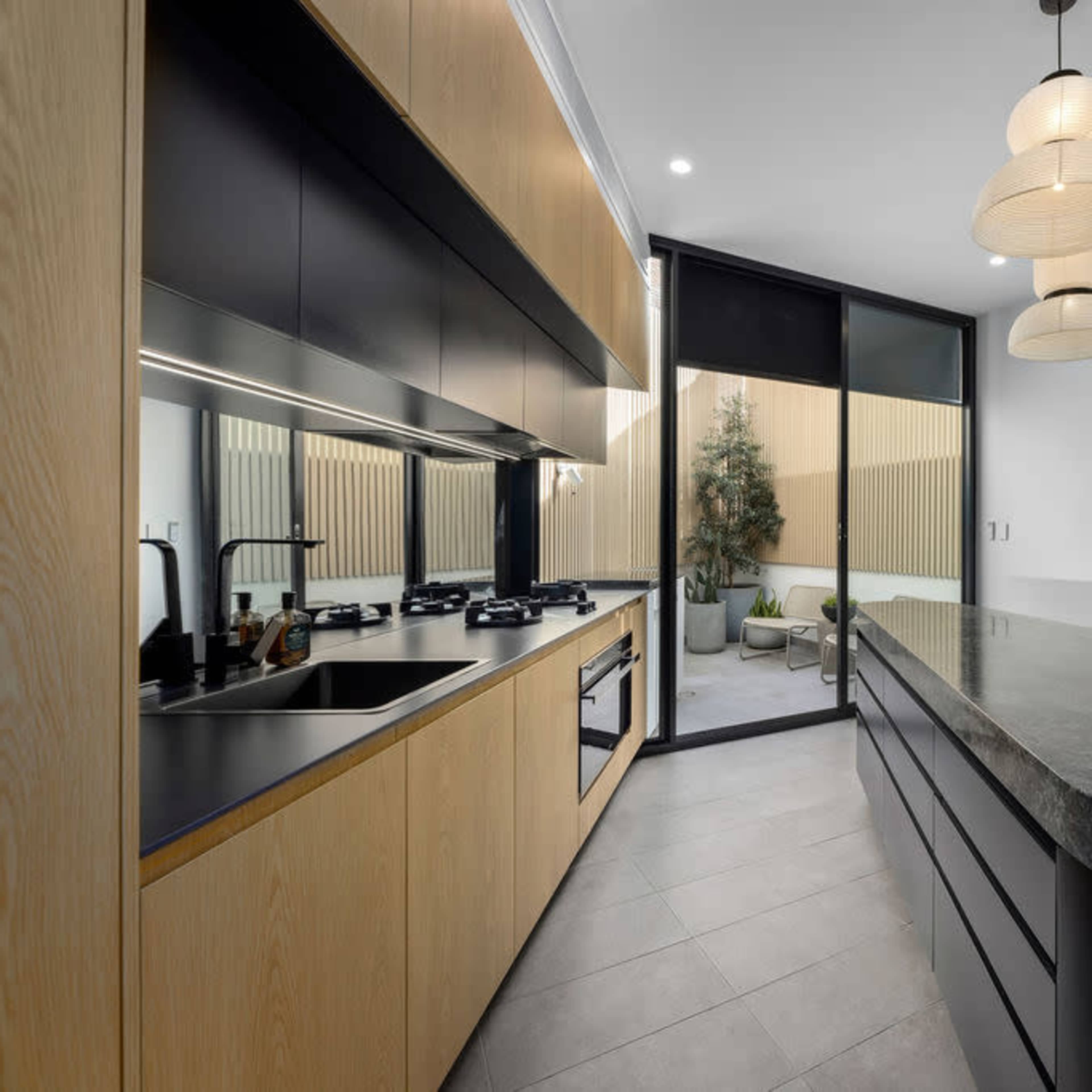 A modern kitchen with wooden cabinets, a dark granite countertop, and large glass doors leading to a patio area.