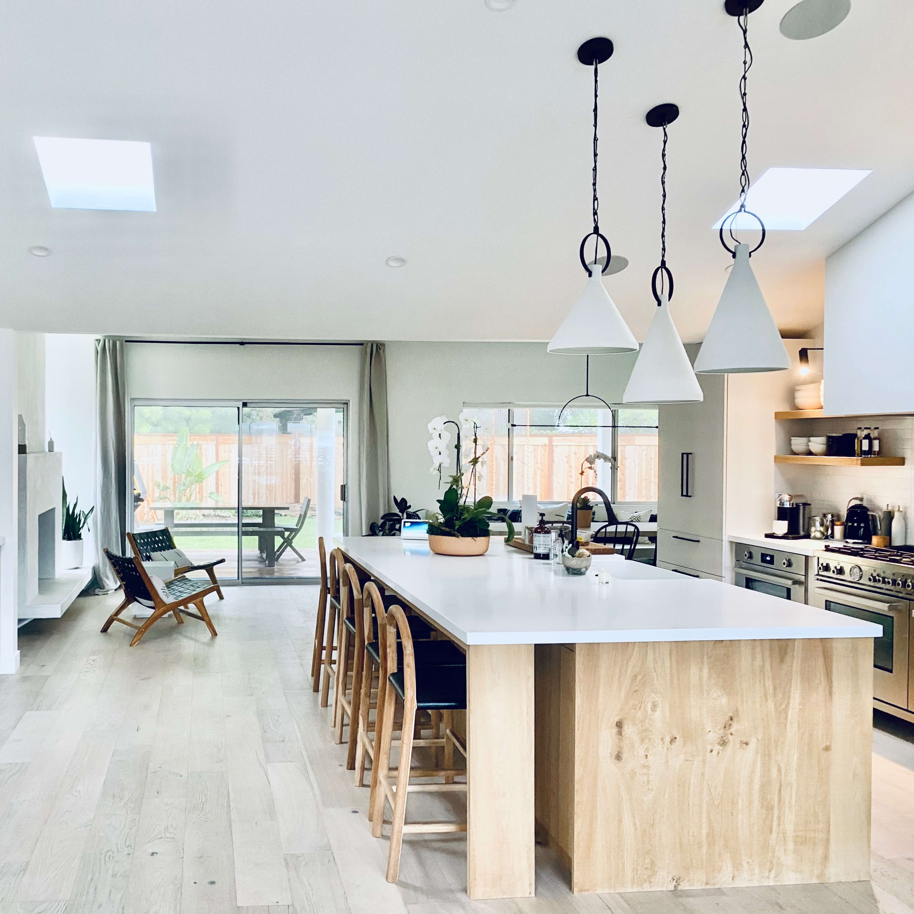 The kitchen features a central island with wooden accents, pendant lighting, and an open layout leading to a patio area.
