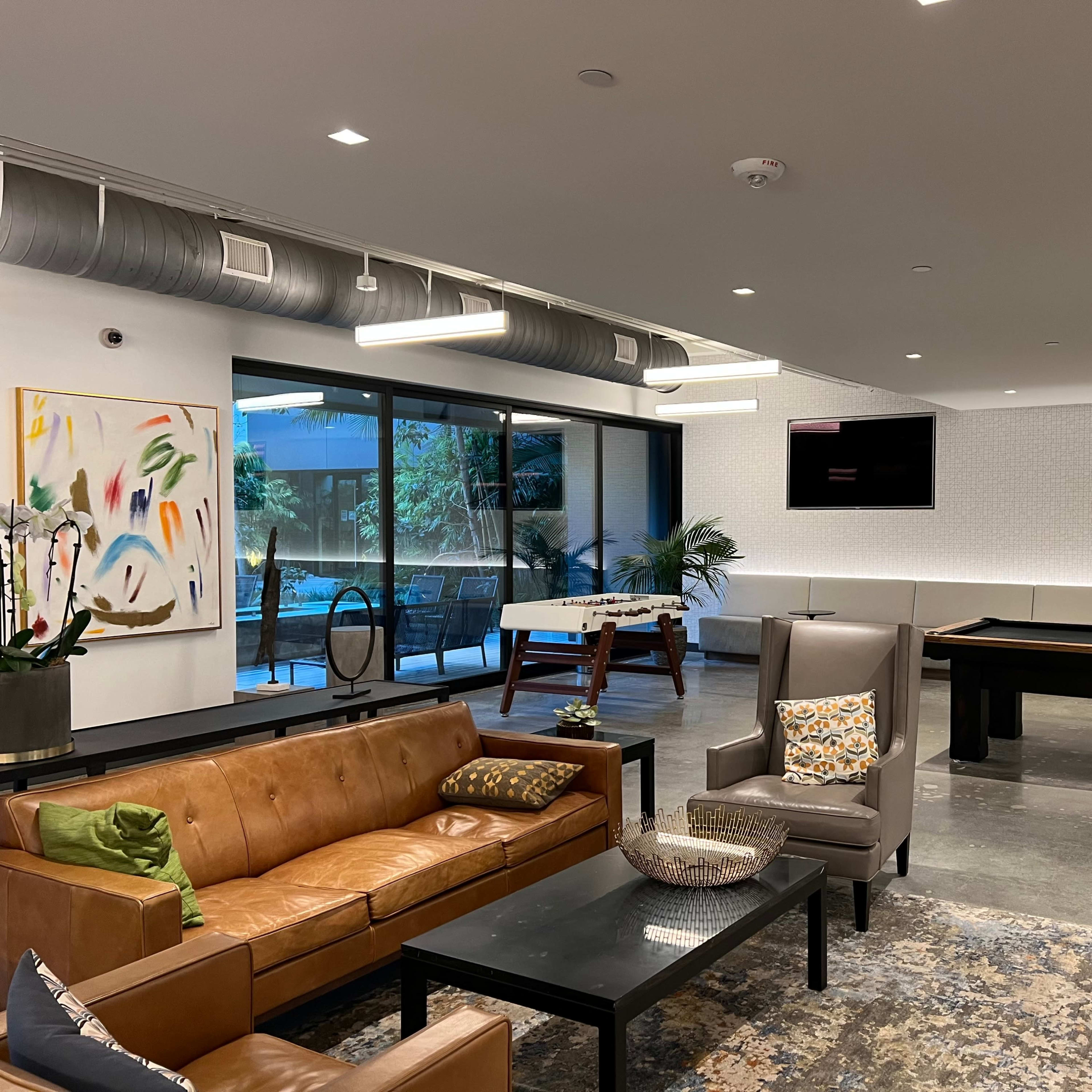 A modern lounge area with leather seating, a pool table, and large windows overlooking an outdoor space.
