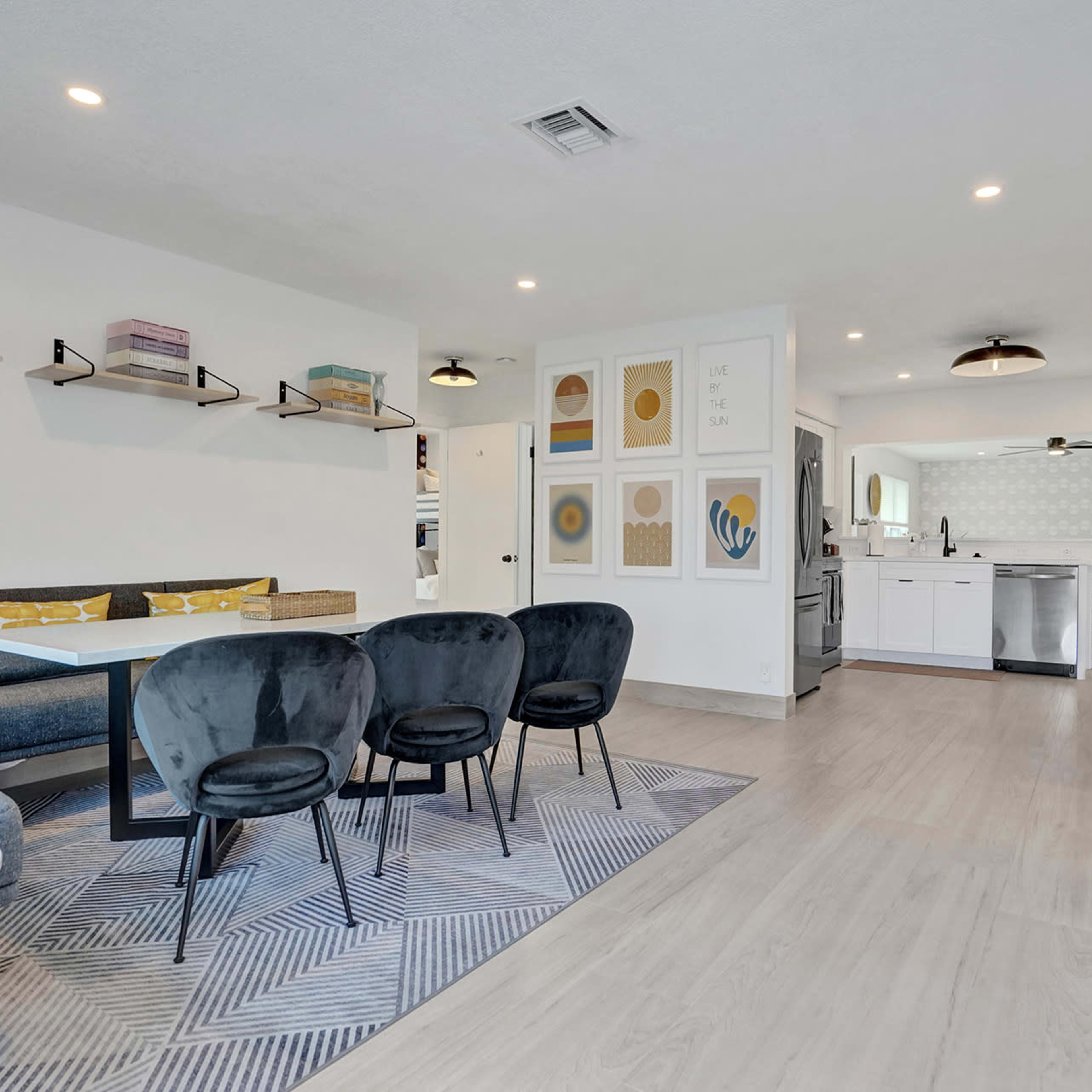 A modern, open-concept living and dining area with a sectional sofa, a round coffee table, a rectangular dining table with chairs, and a kitchen in the background.