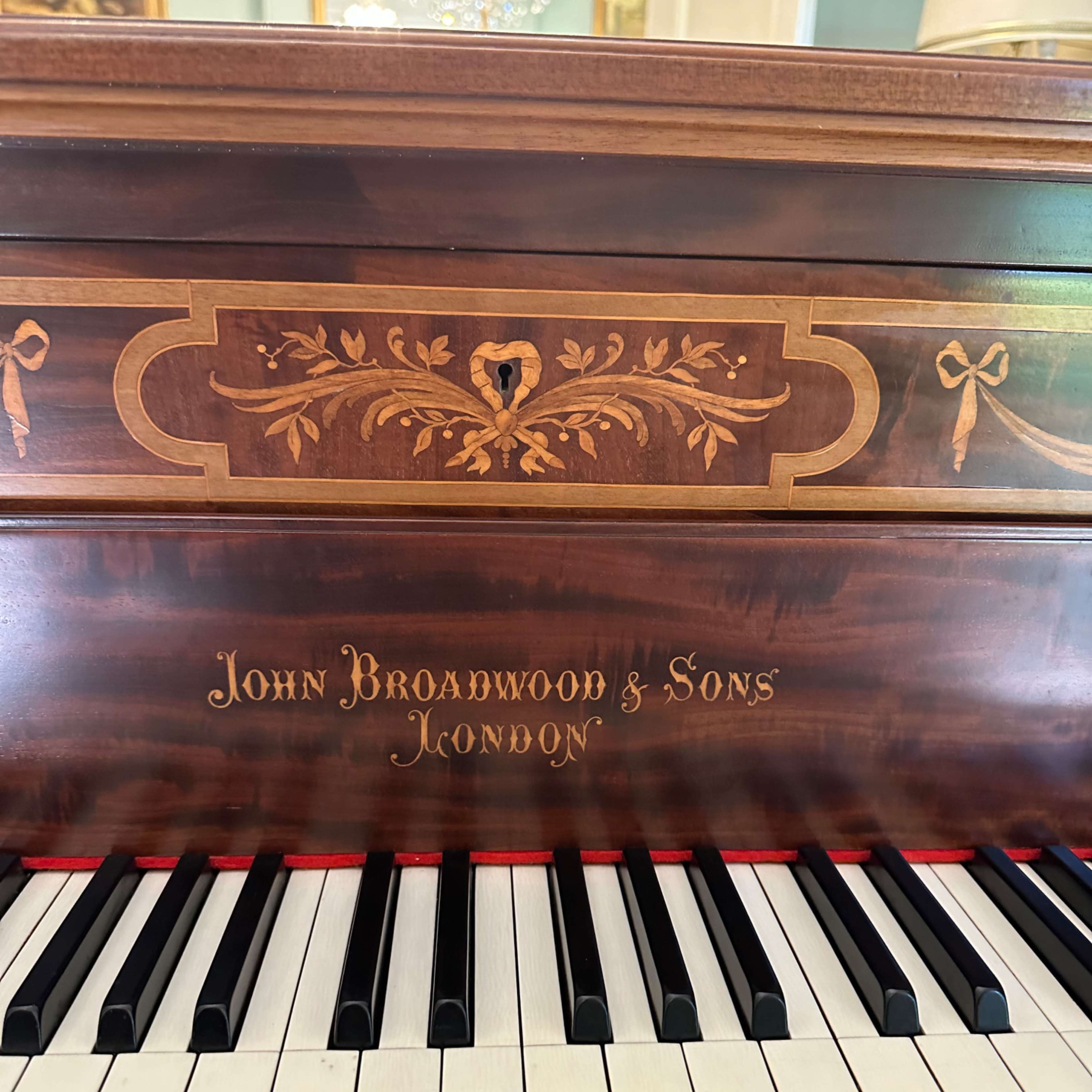 The keyboard of a wooden piano with the inscription "John Broadwood & Sons London" and ornate carvings on the front panel.
