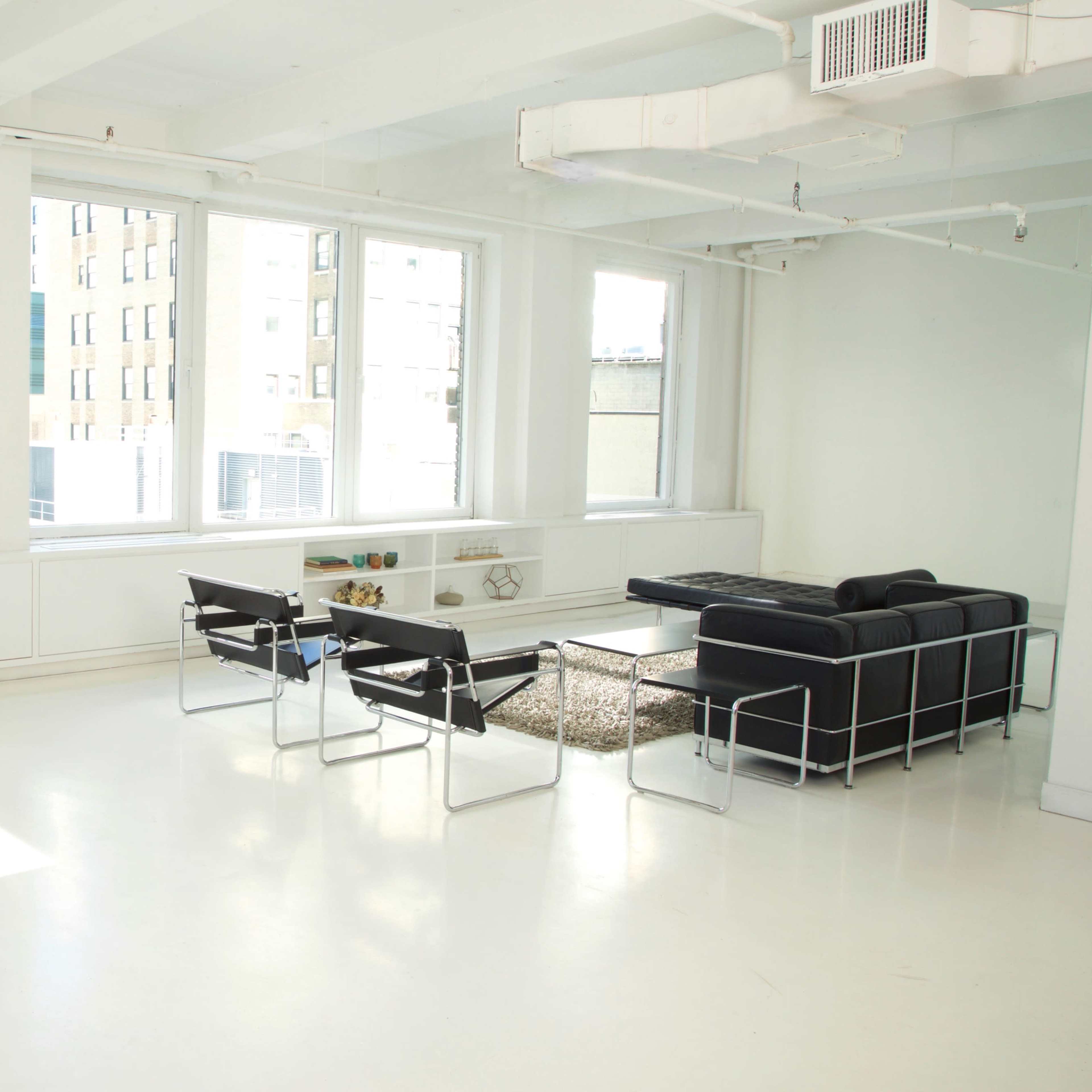 A spacious, bright room features large windows, modern black furniture, and a minimalist design.