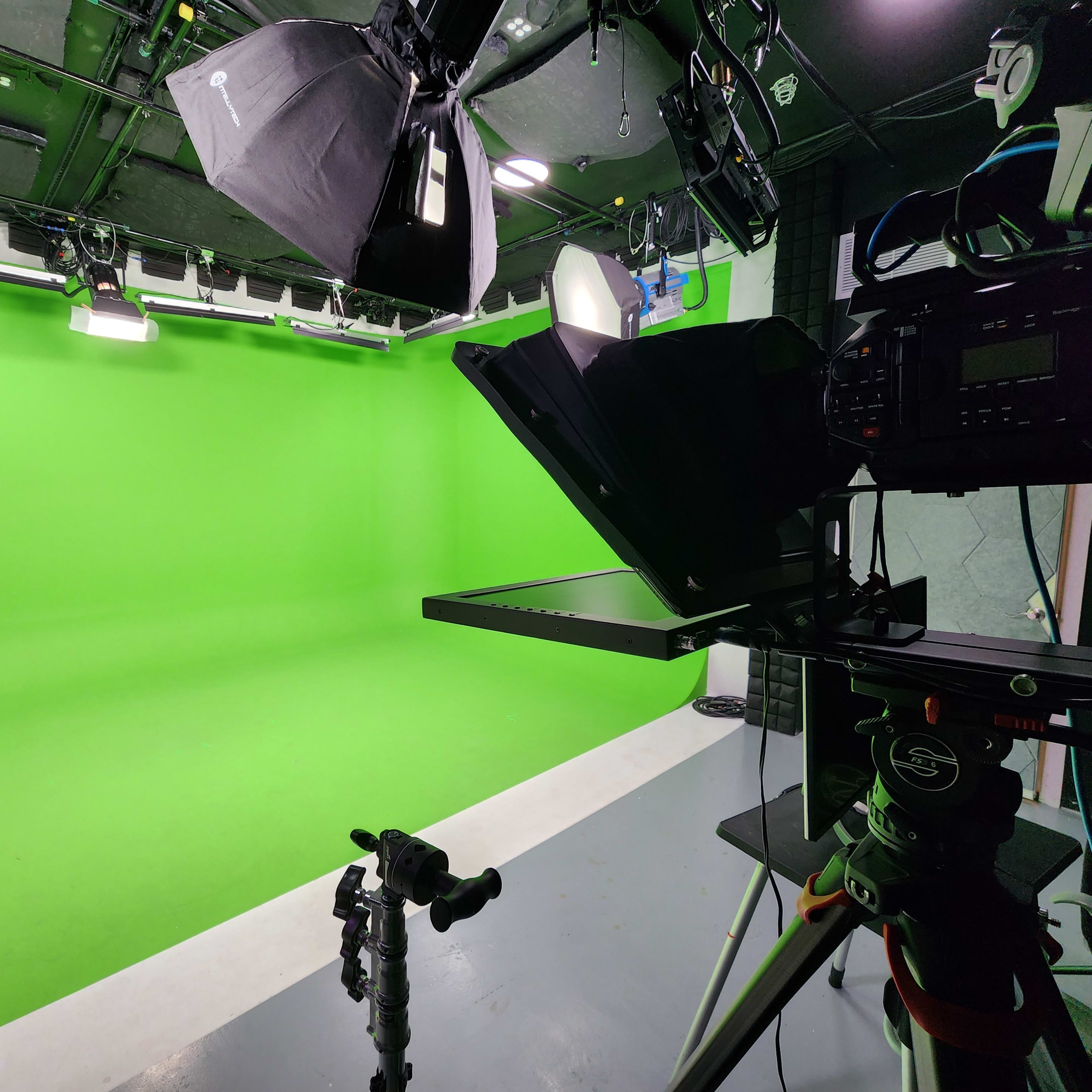 A green screen studio with lighting equipment and a camera setup on a tripod.