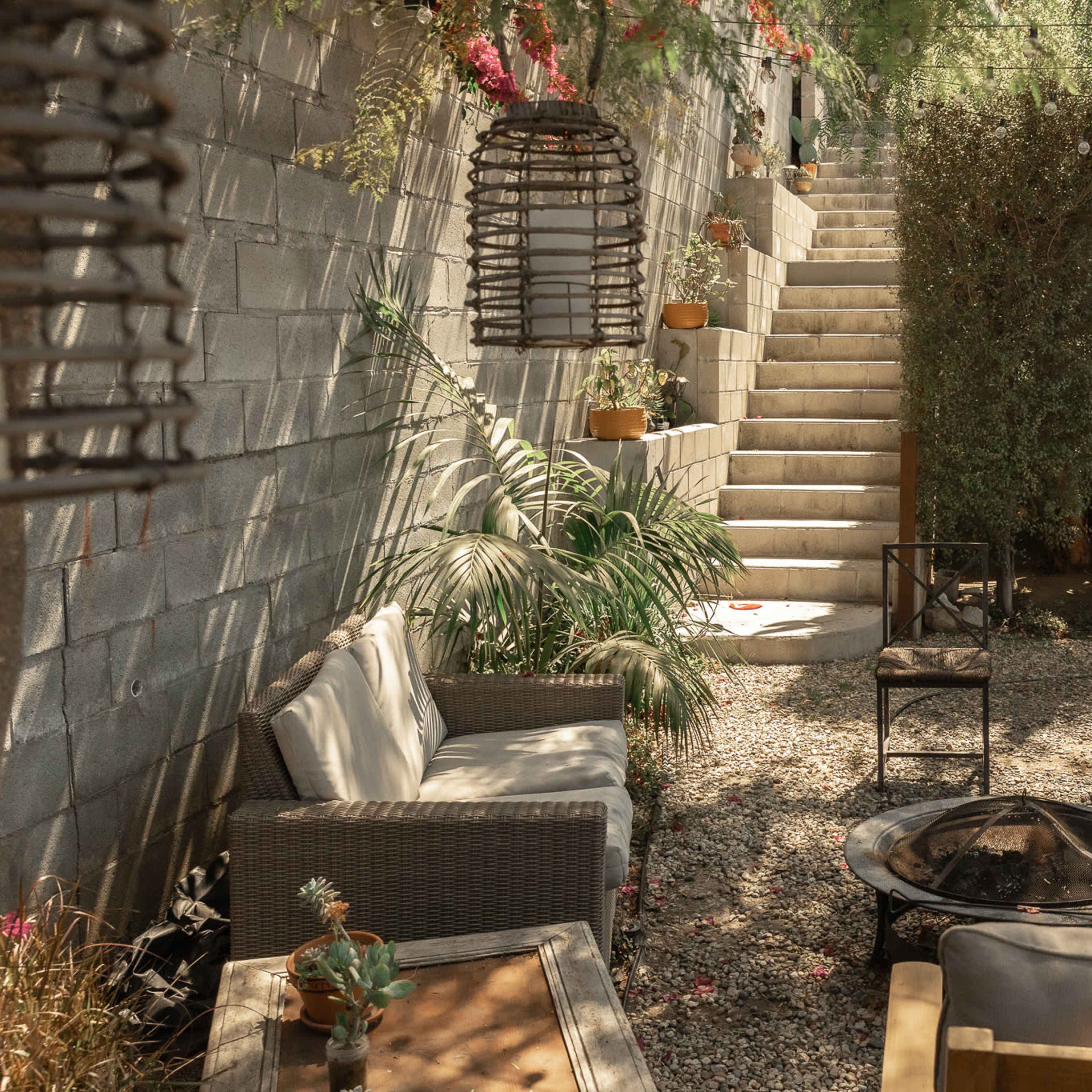 A cozy garden area with seating arrangements, a fire pit, and stairs leading to an elevated section surrounded by greenery.