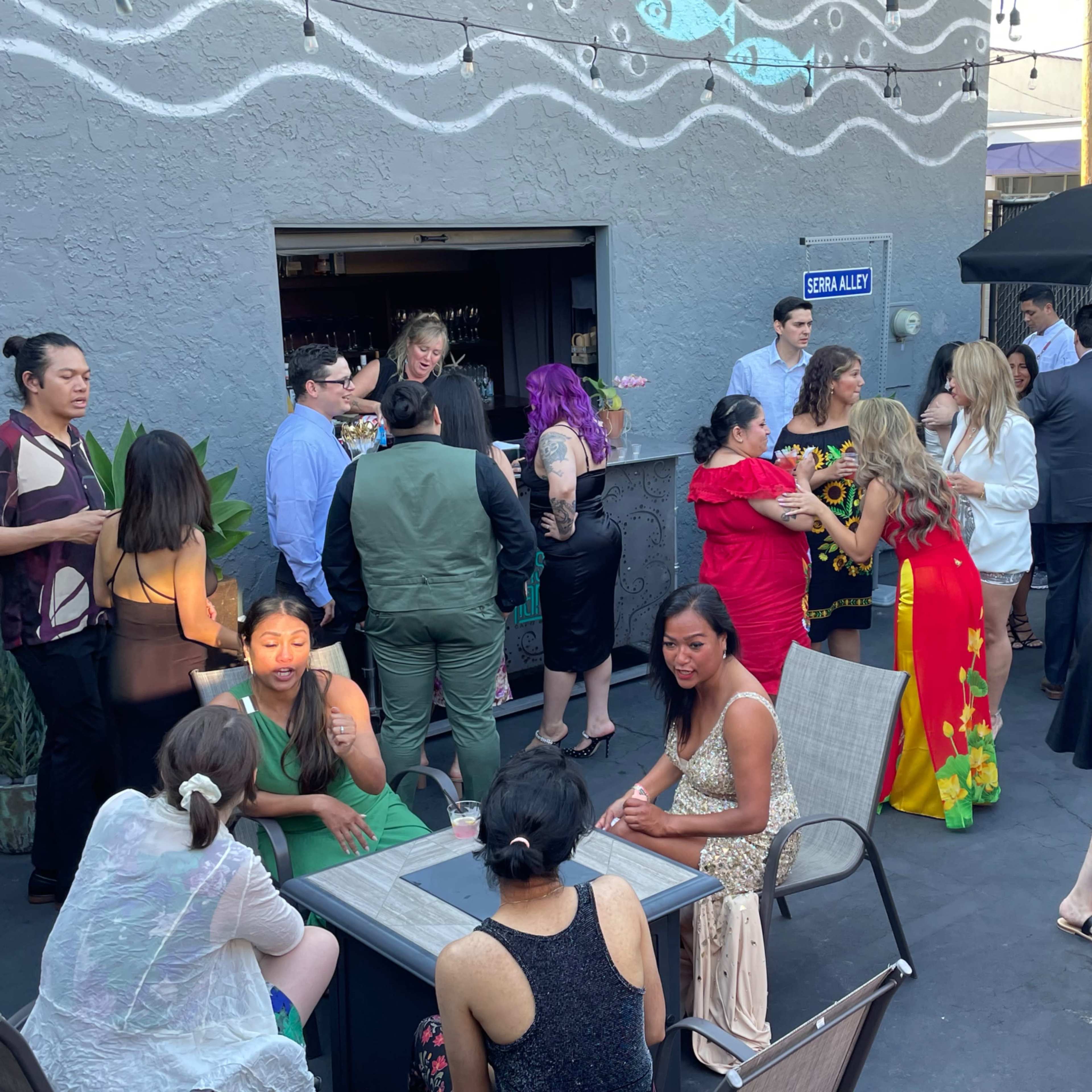 A group of people socialize at an outdoor event, with some standing and others seated around tables.