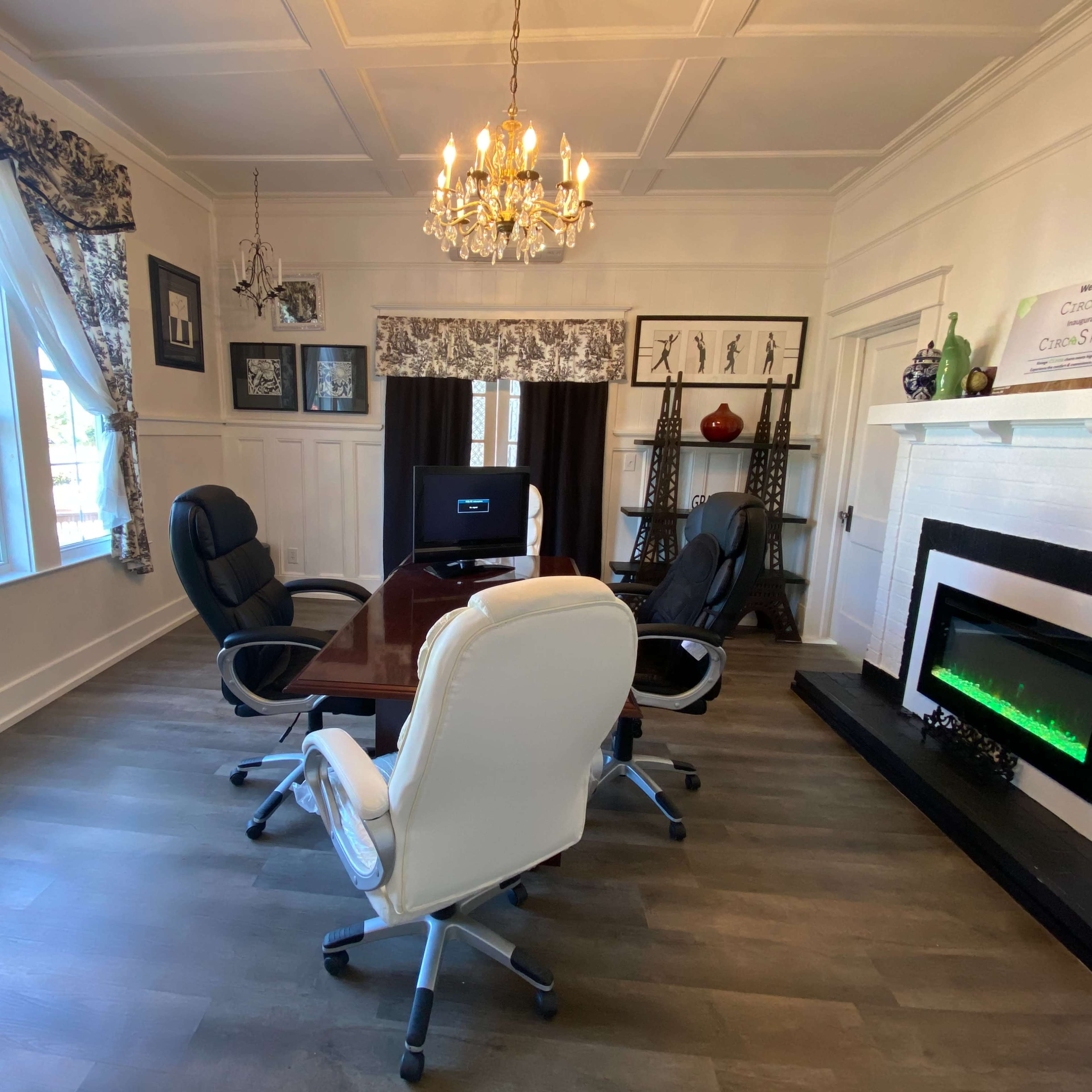 A well-lit office with a wooden conference table surrounded by four ergonomic chairs and a decorative electric fireplace against the wall.
