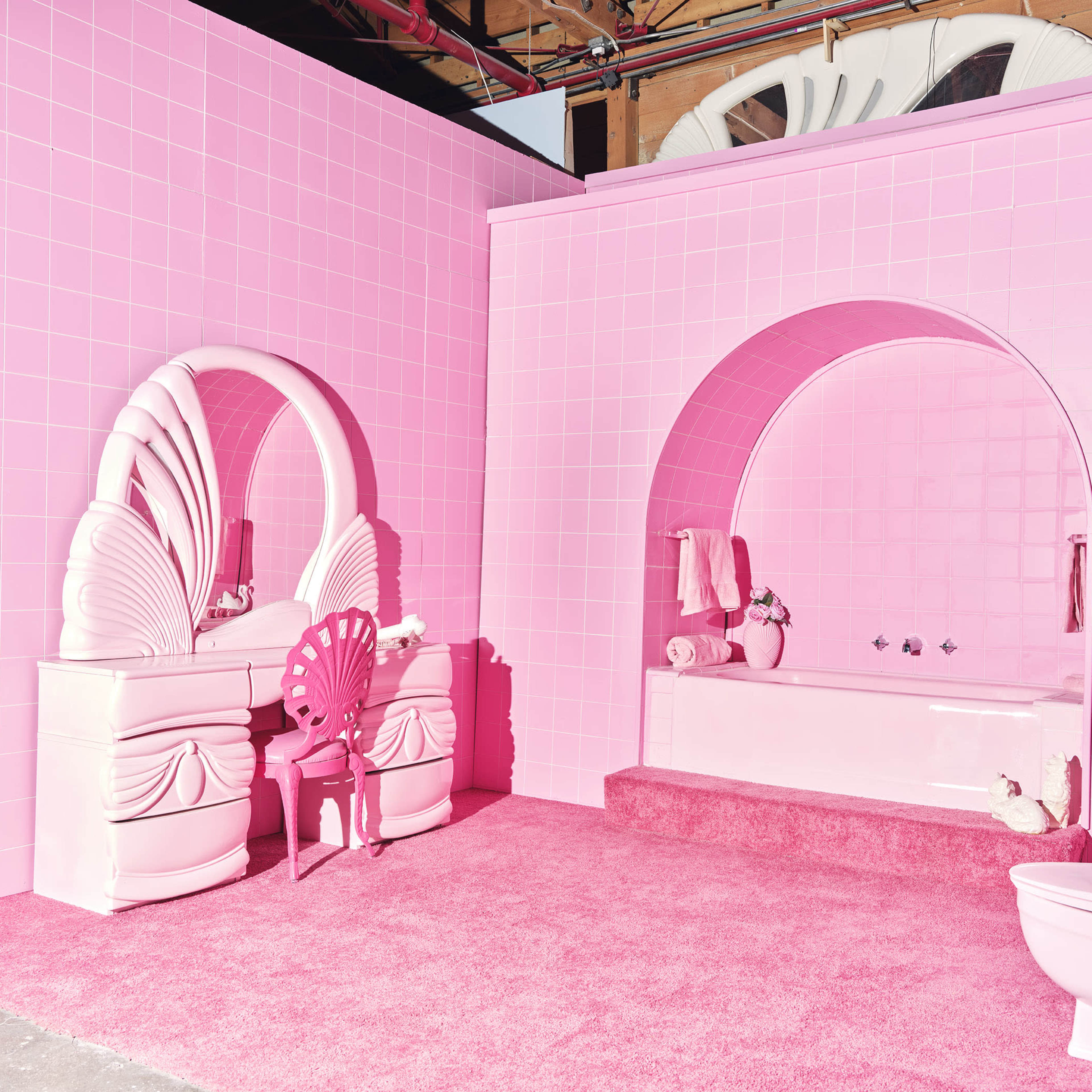 A pink bathroom featuring a bathtub, mirrors, a vanity, and a toilet, all set against bright pink tiled walls and carpet.